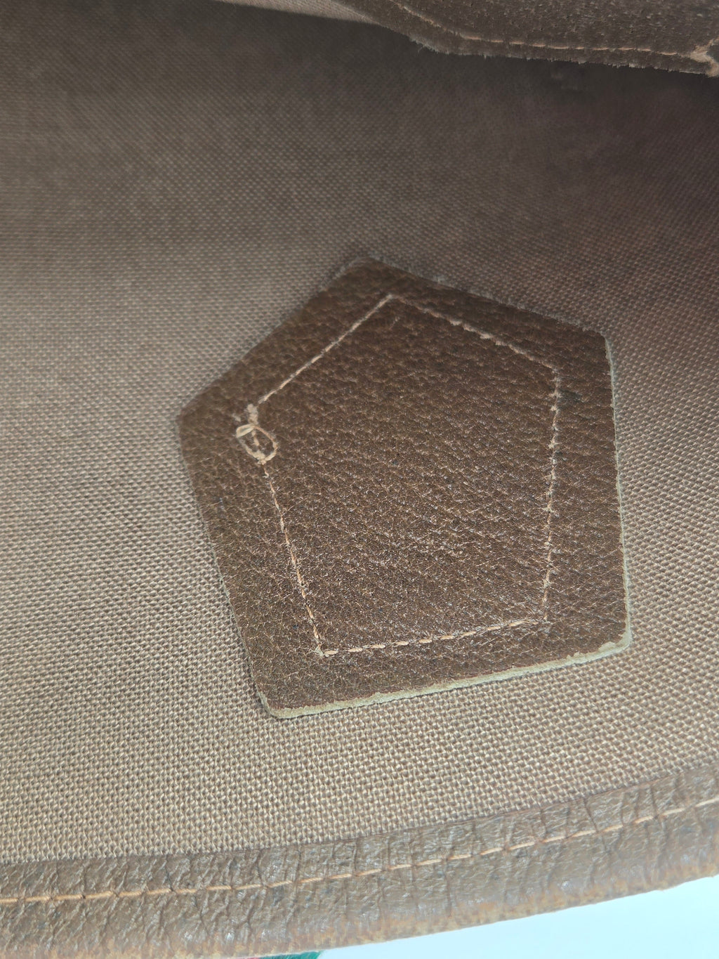 Close-up of a brown hexagonal leather patch with white stitching on a textured brown fabric background.