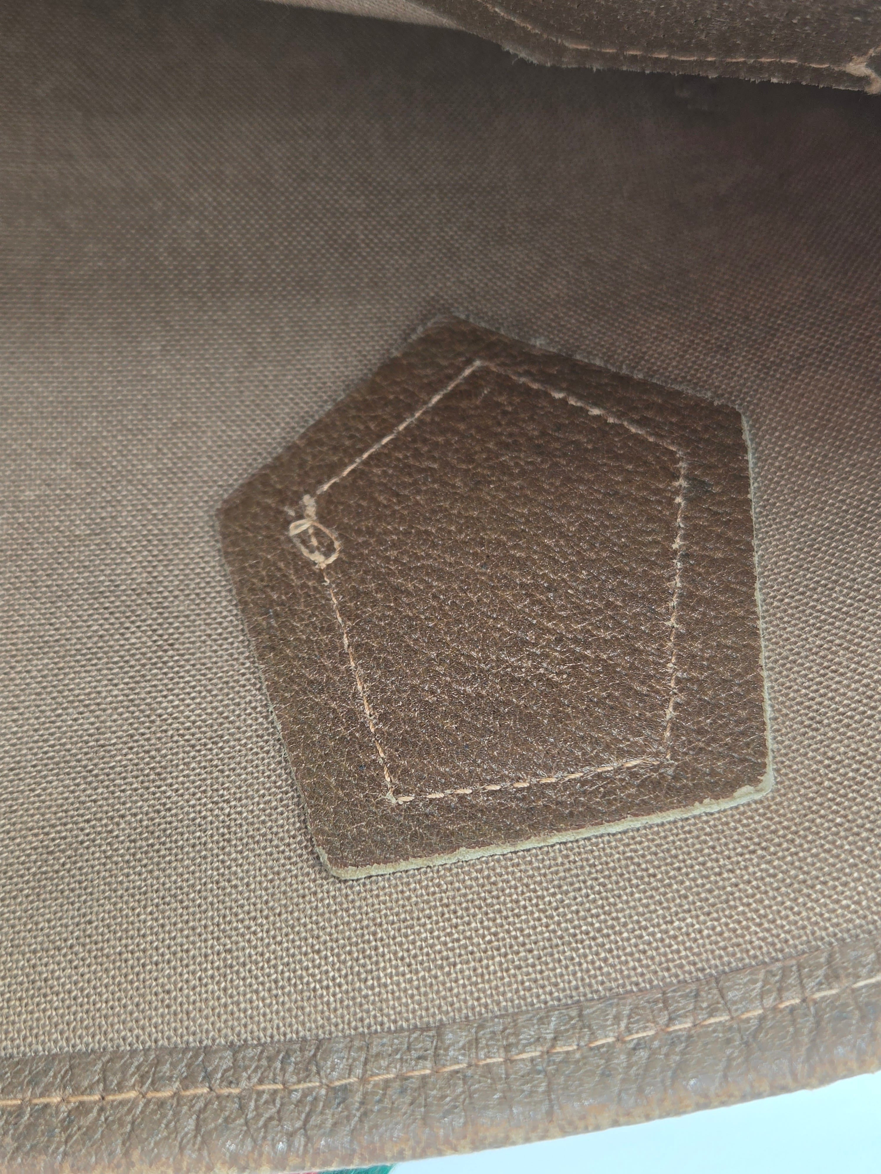 Close-up of a brown hexagonal leather patch with white stitching on a textured brown fabric background.