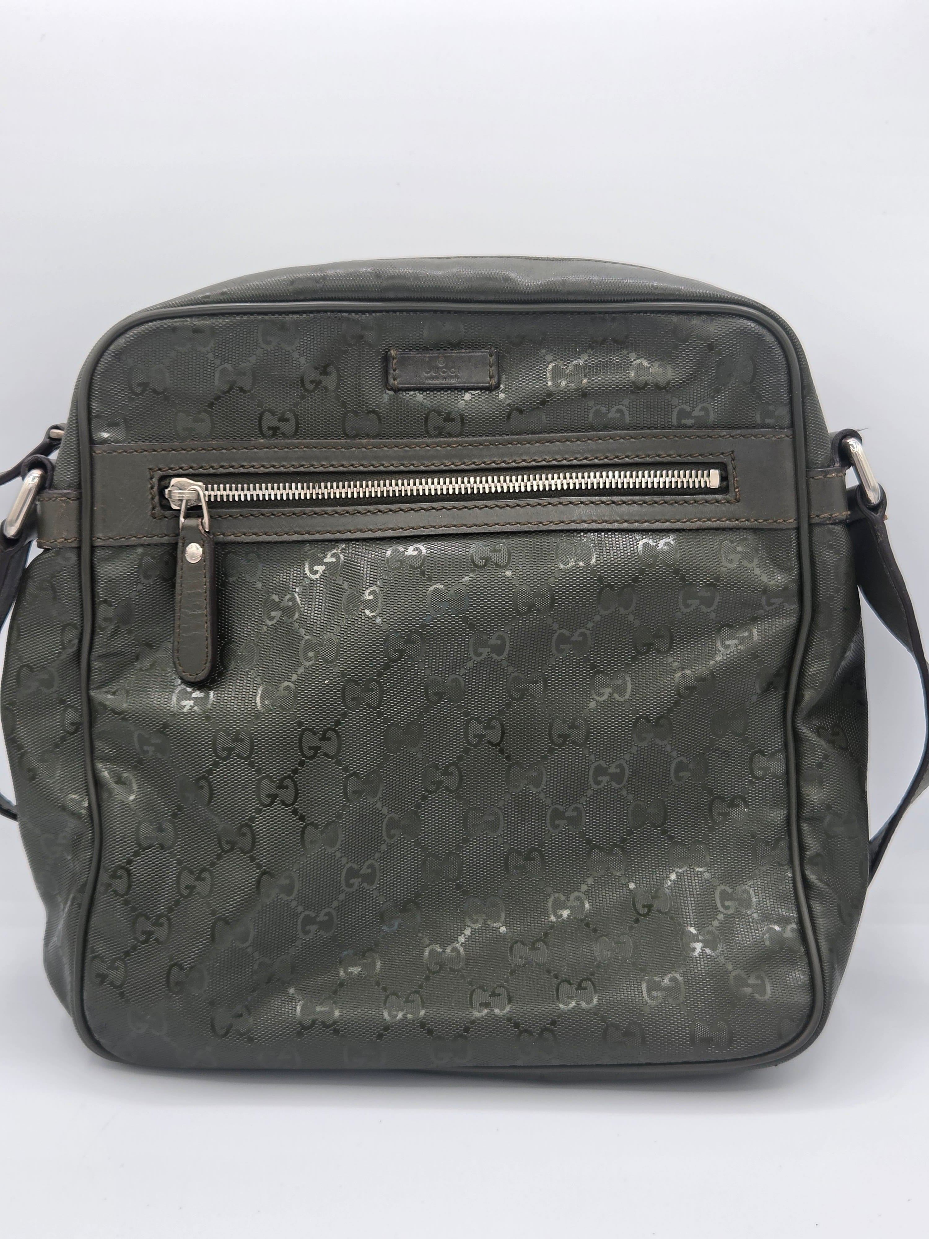 A dark gray Gucci backpack with the brand's signature GG monogram pattern, featuring a vertical zippered pocket on the front and a top handle, shown against a plain white background.