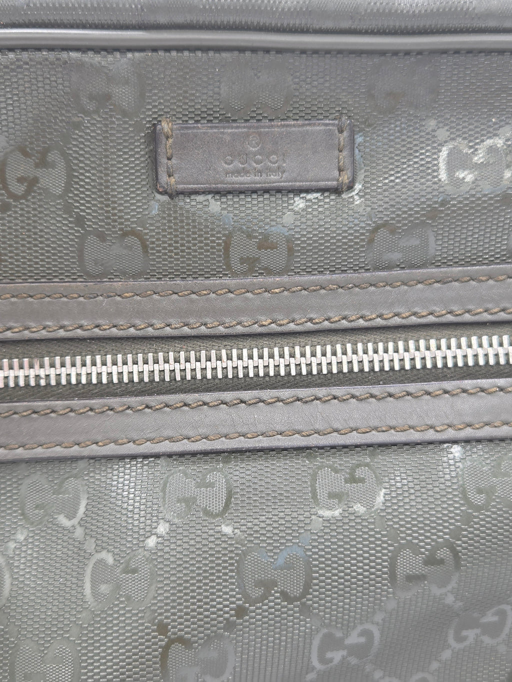 Close-up of a gray Gucci monogram canvas bag with a silver zipper and a branded leather patch.