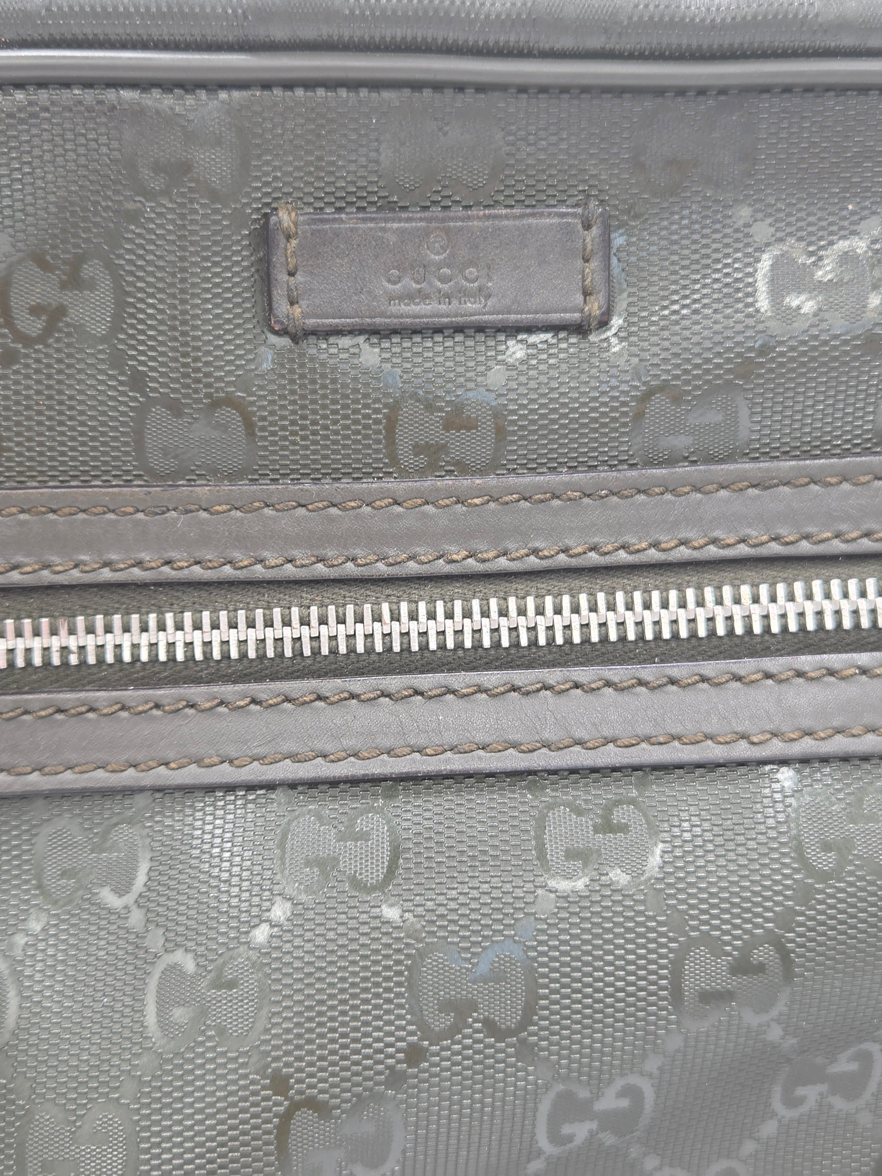 Close-up of a gray Gucci monogram canvas bag with a silver zipper and a branded leather patch.
