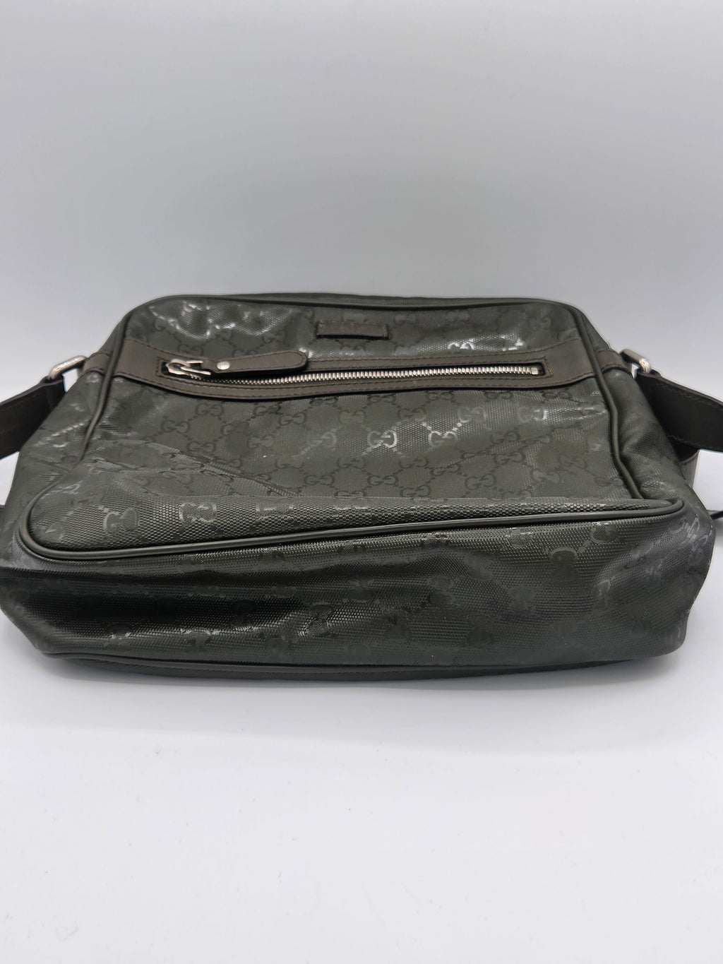 A dark gray Gucci crossbody bag with the brand's signature GG monogram pattern, featuring a front zippered pocket and a side zipper, shown against a plain light gray background.