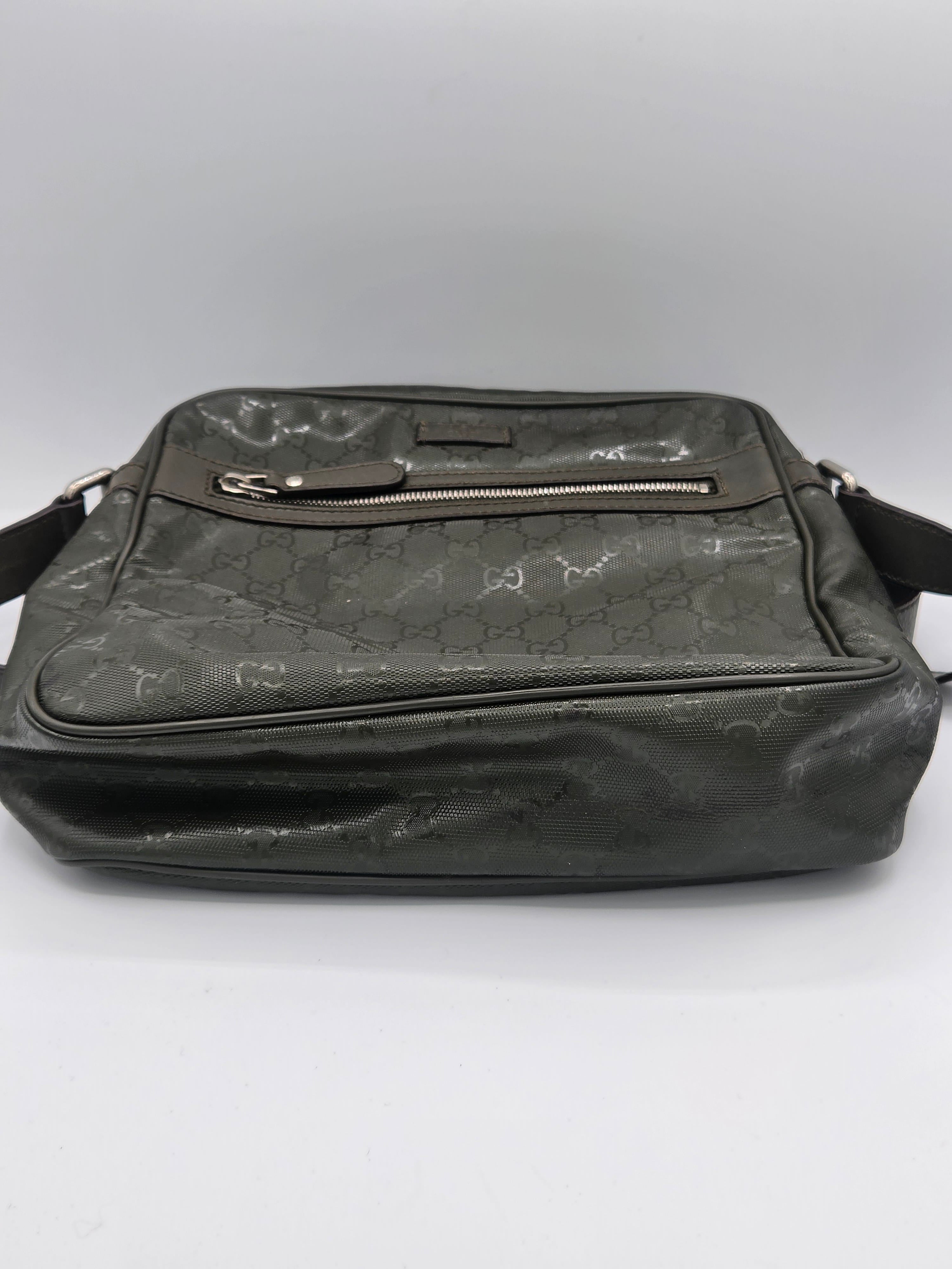 A dark gray Gucci crossbody bag with the brand's signature GG monogram pattern, featuring a front zippered pocket and a side zipper, shown against a plain light gray background.