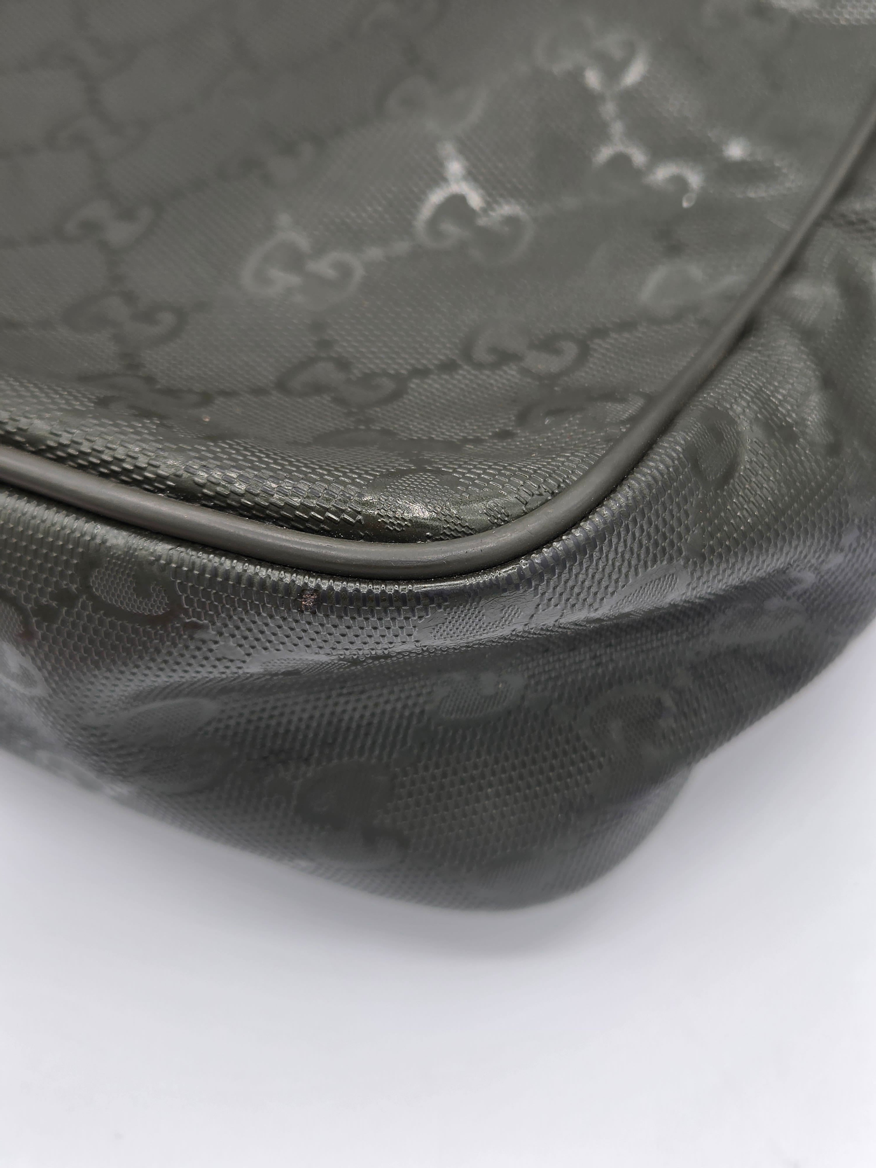 Close-up of a dark gray Gucci monogram coated canvas bag corner with a black leather trim on a white background.
