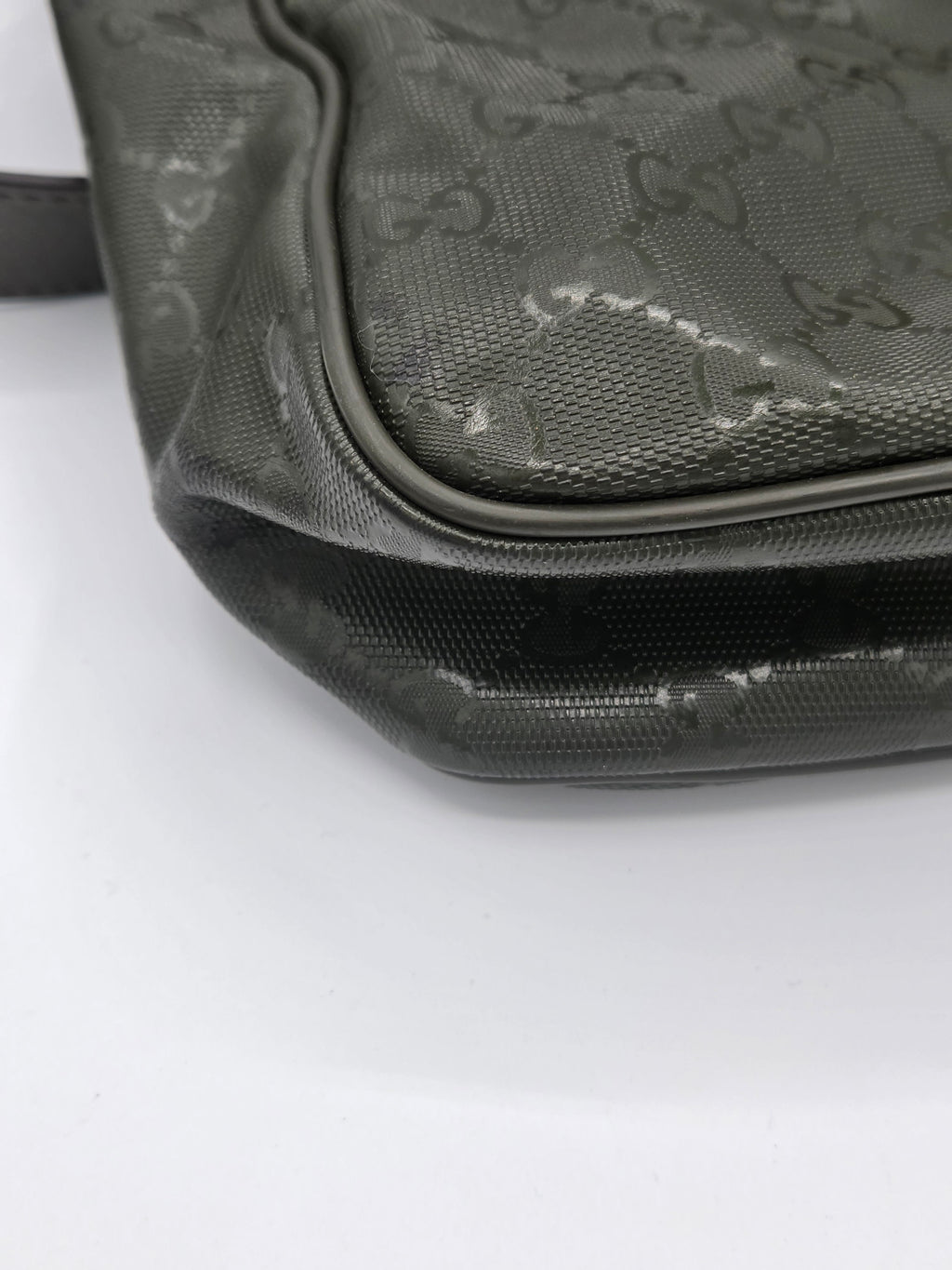 Close-up of a dark gray Gucci monogram coated canvas bag corner with black trim on a white background.