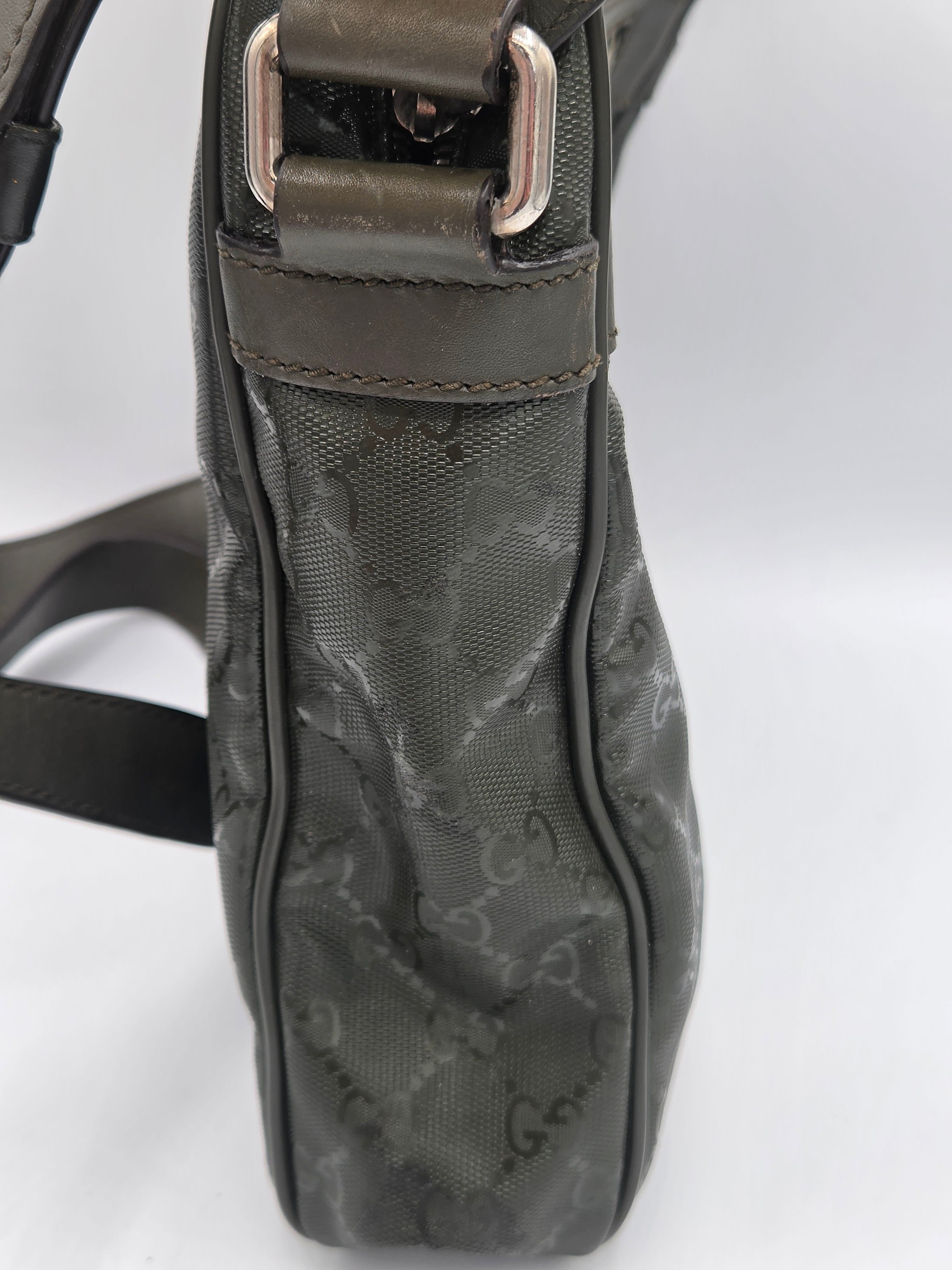 A close-up of a dark gray Gucci shoulder bag featuring the brand's signature GG monogram canvas and a dark brown leather strap with a silver-tone buckle.