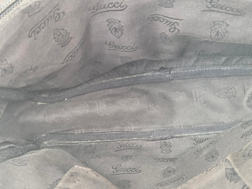 Close-up of a dark gray Gucci fabric lining with an allover embossed logo pattern and a zippered pocket.