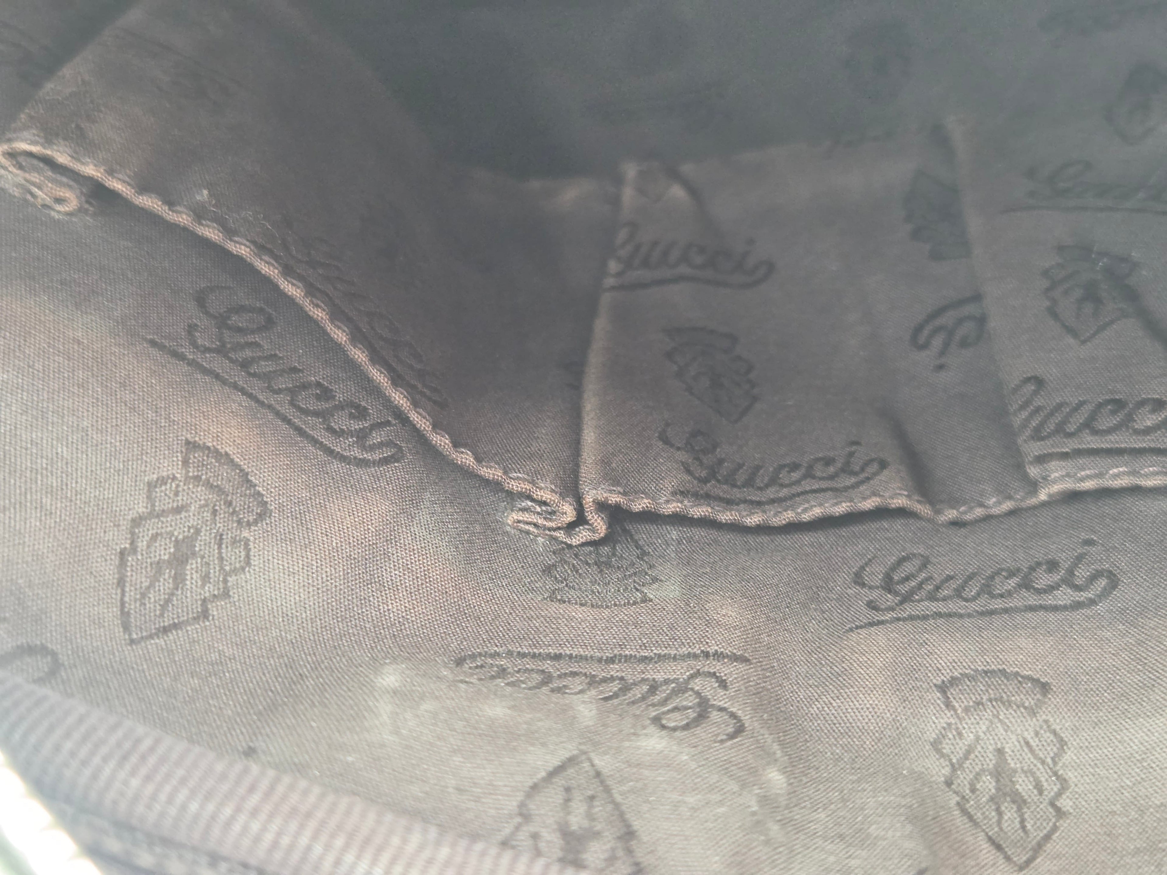 Close-up of a dark gray Gucci fabric with an allover embossed logo pattern and stitched details.