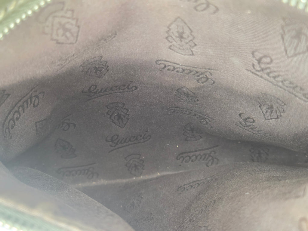 Close-up of the interior lining of a Gucci pouch or bag, showing a dark gray suede-like fabric with an all-over embossed Gucci logo pattern.