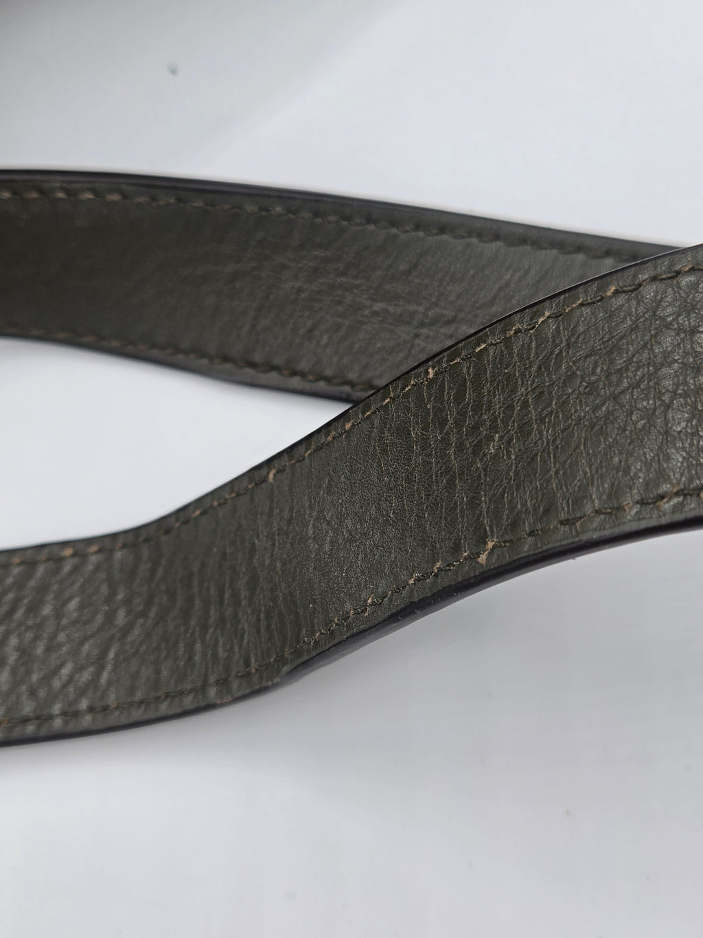 A close-up of a dark gray pebbled leather strap, likely a camera strap or belt, showing detailed stitching on a plain white background.