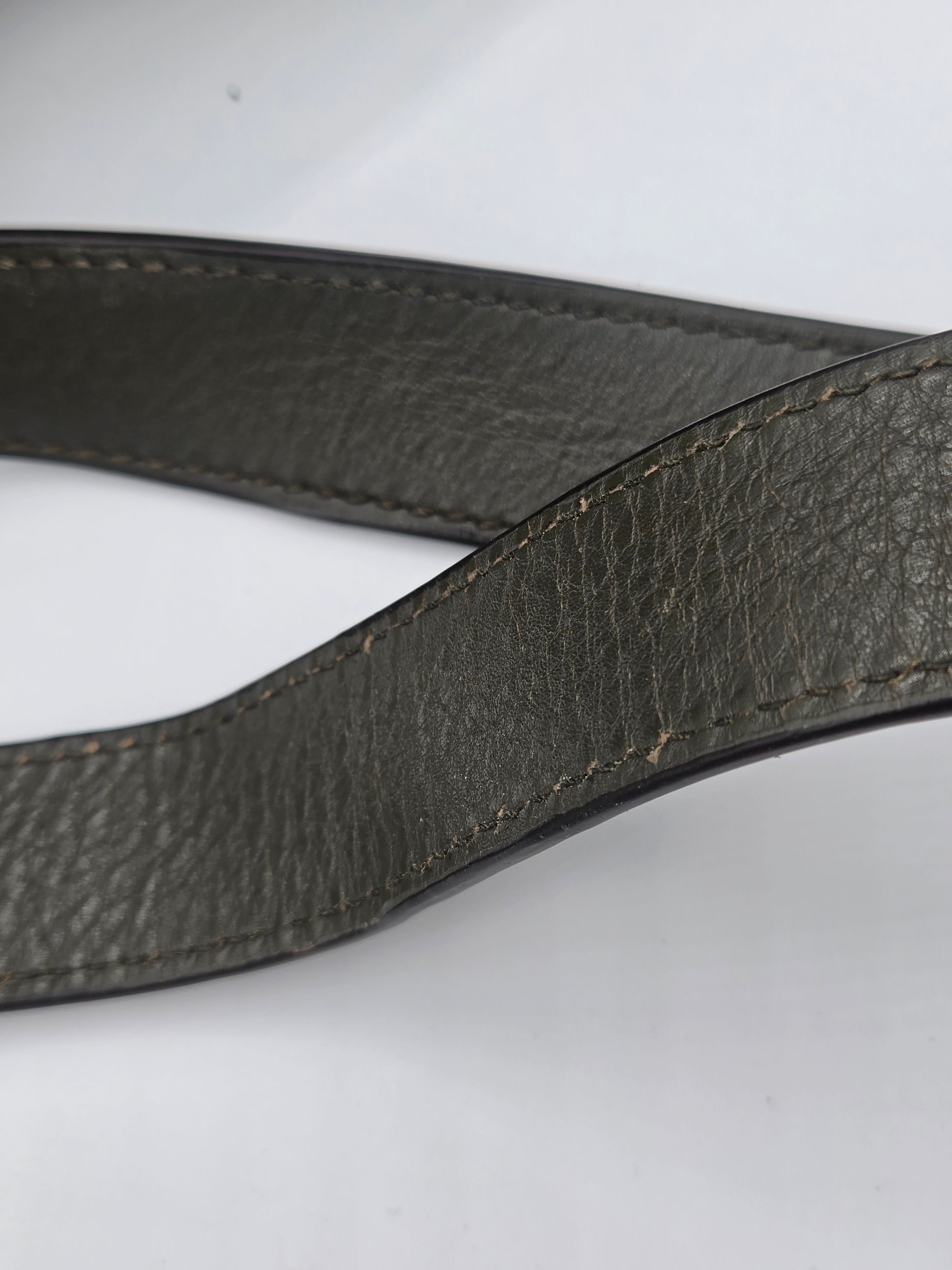 A close-up of a dark gray pebbled leather strap, likely a camera strap or belt, showing detailed stitching on a plain white background.