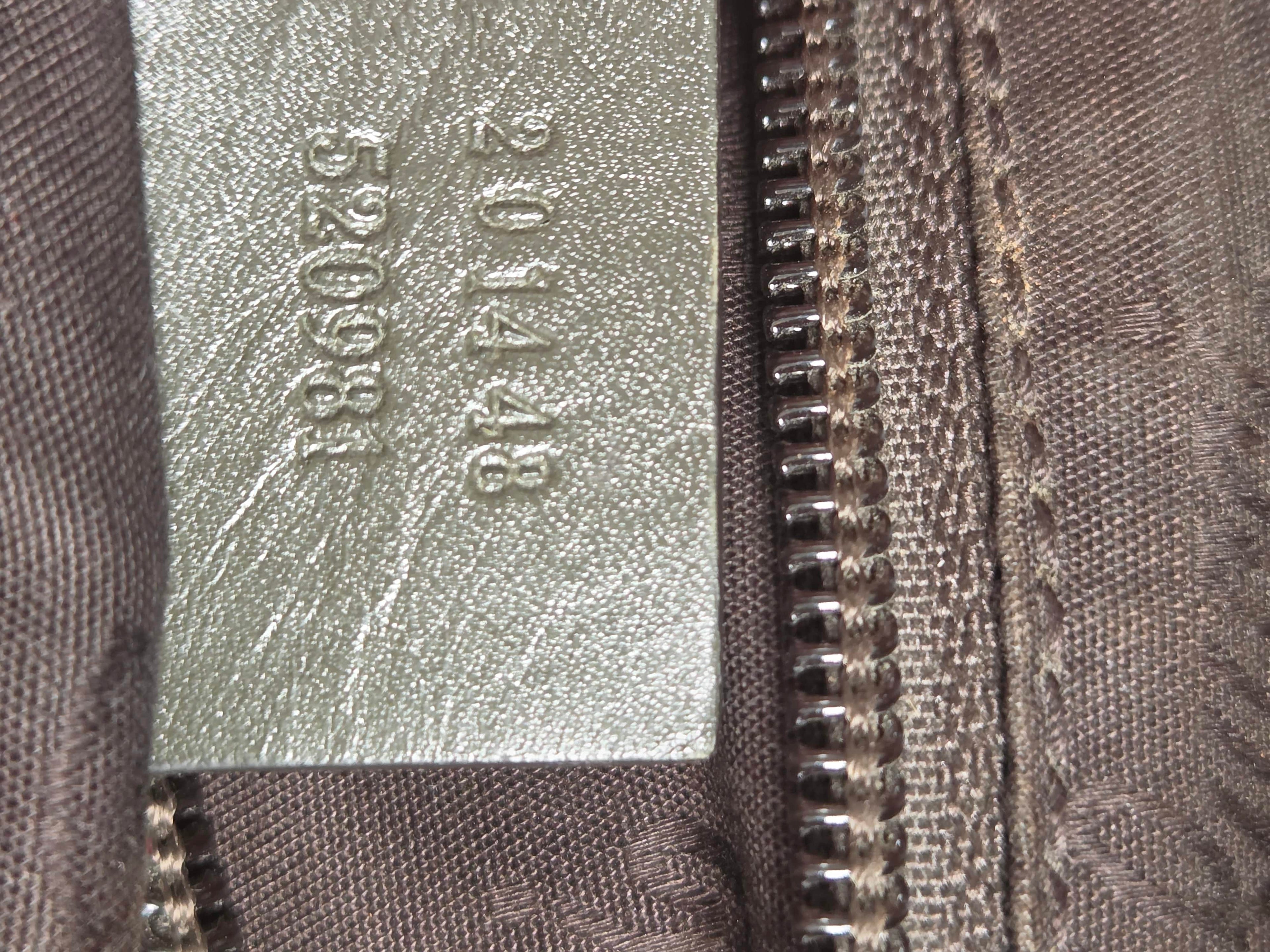 Close-up of a brown textured fabric zipper with a silver metallic tag embossed with numbers.