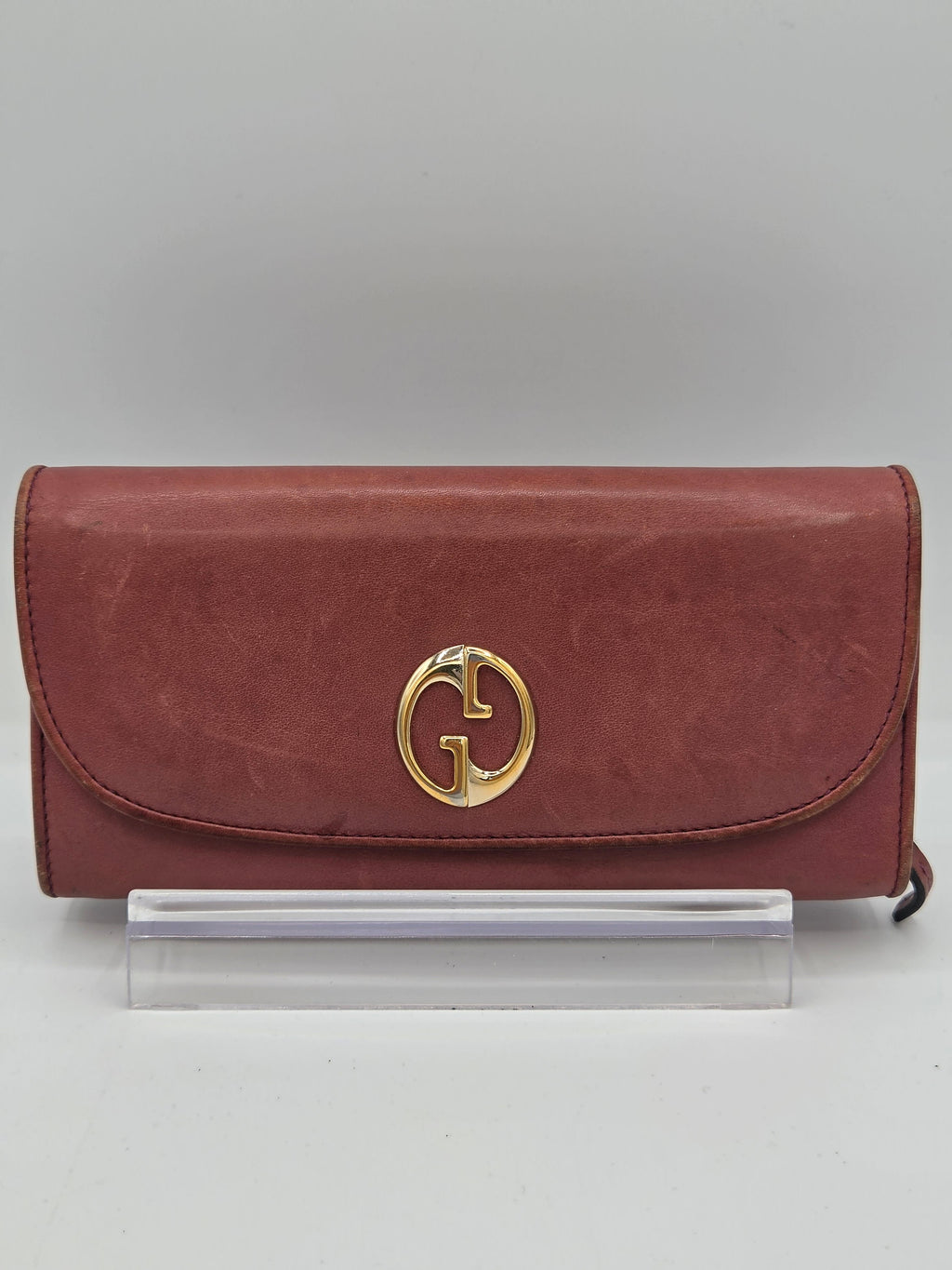 A vintage red leather clutch bag with a gold-tone interlocking G logo on the front, displayed on a clear acrylic stand against a neutral gray background.