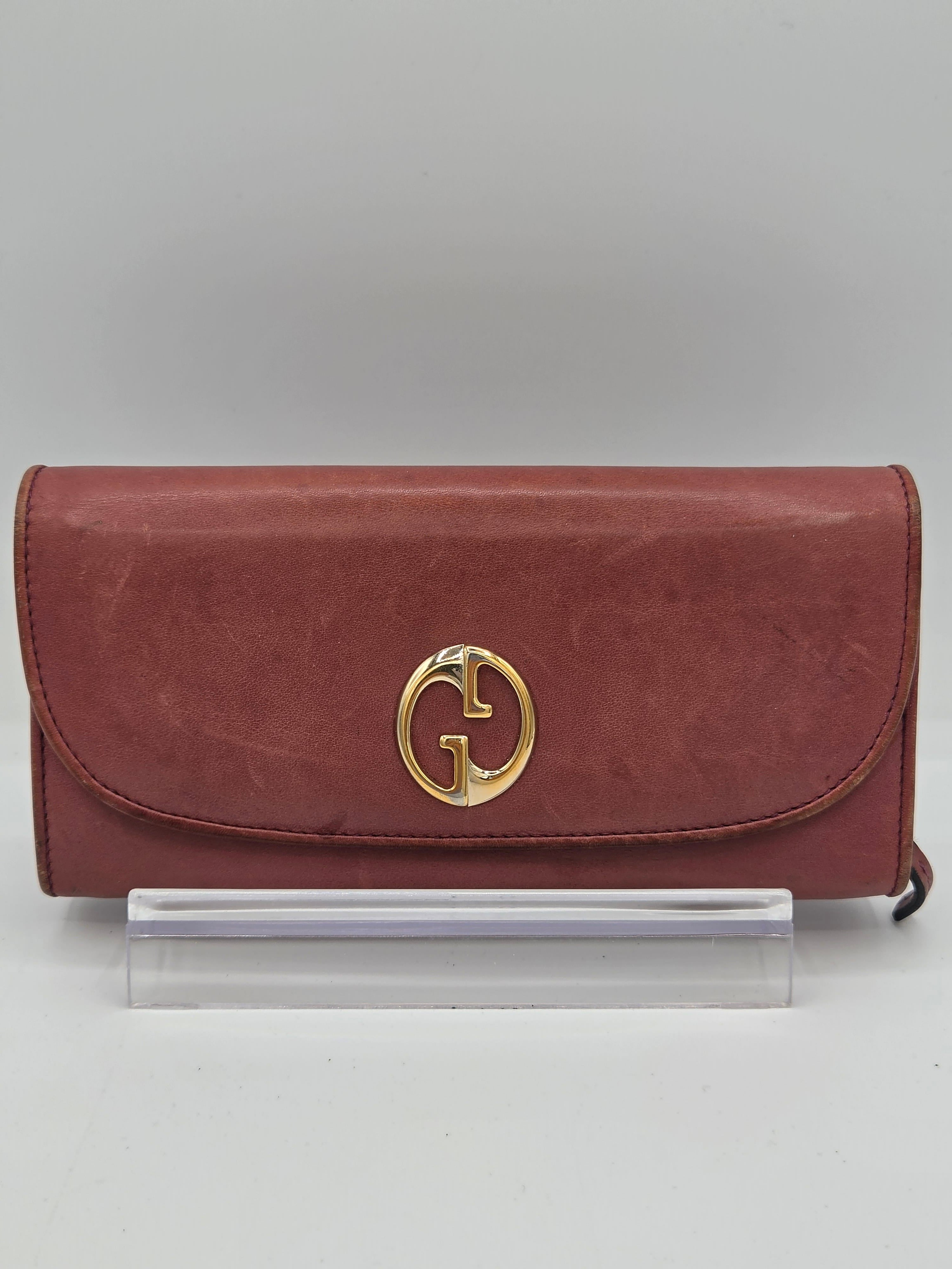A vintage red leather clutch bag with a gold-tone interlocking G logo on the front, displayed on a clear acrylic stand against a neutral gray background.