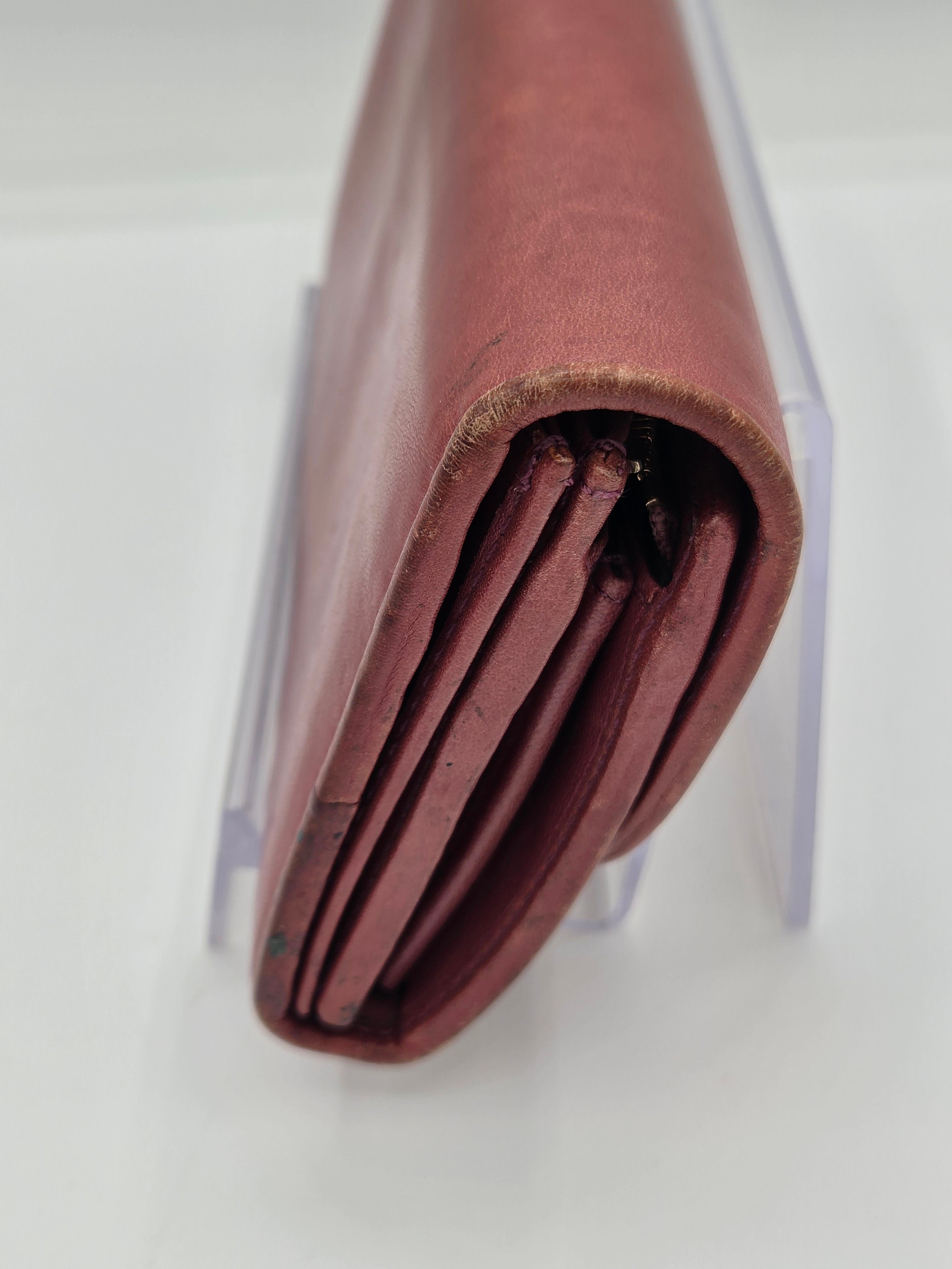 A close-up of a folded reddish-brown leather wallet or folio resting on a clear acrylic stand against a white background.
