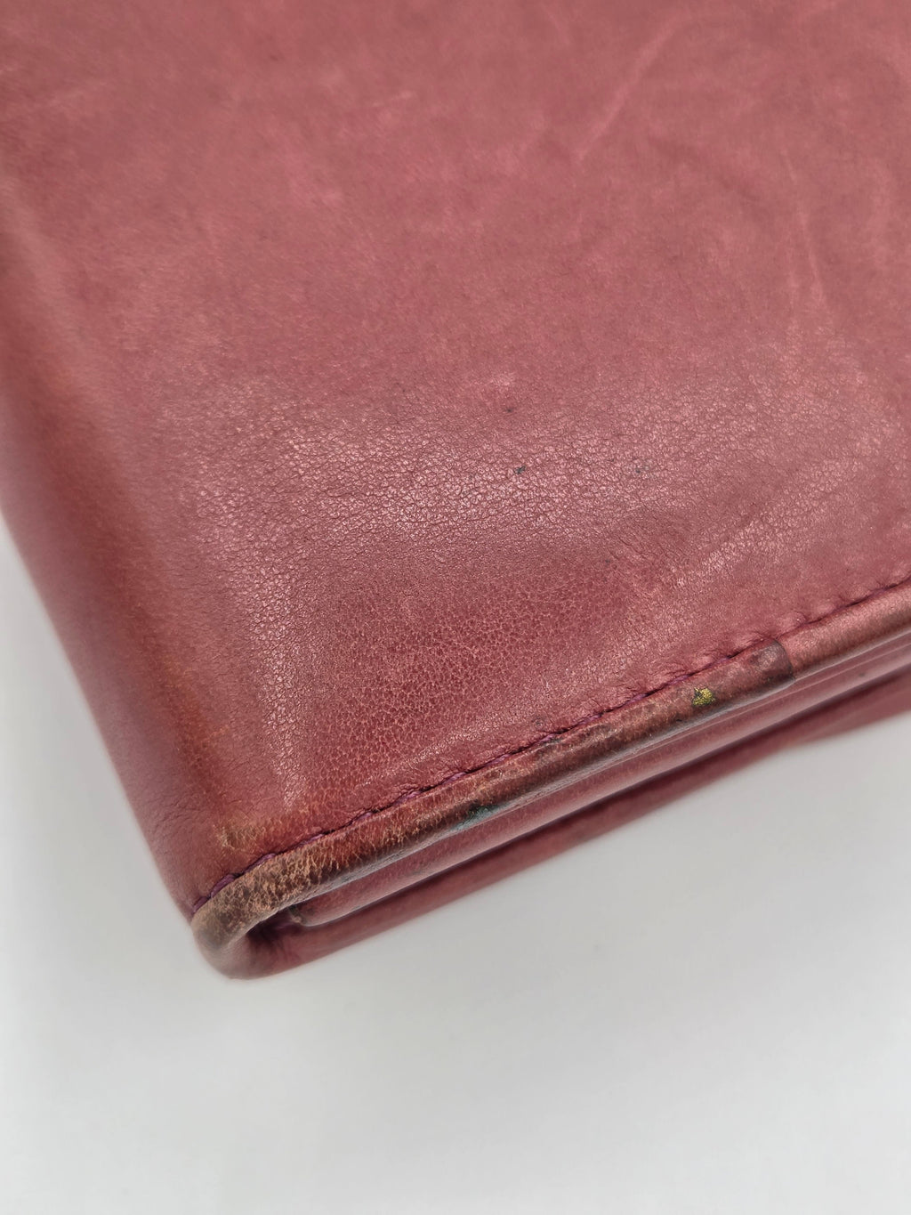 Close-up of a dusty rose or mauve leather wallet corner showing the textured leather surface and stitching against a plain white background.
