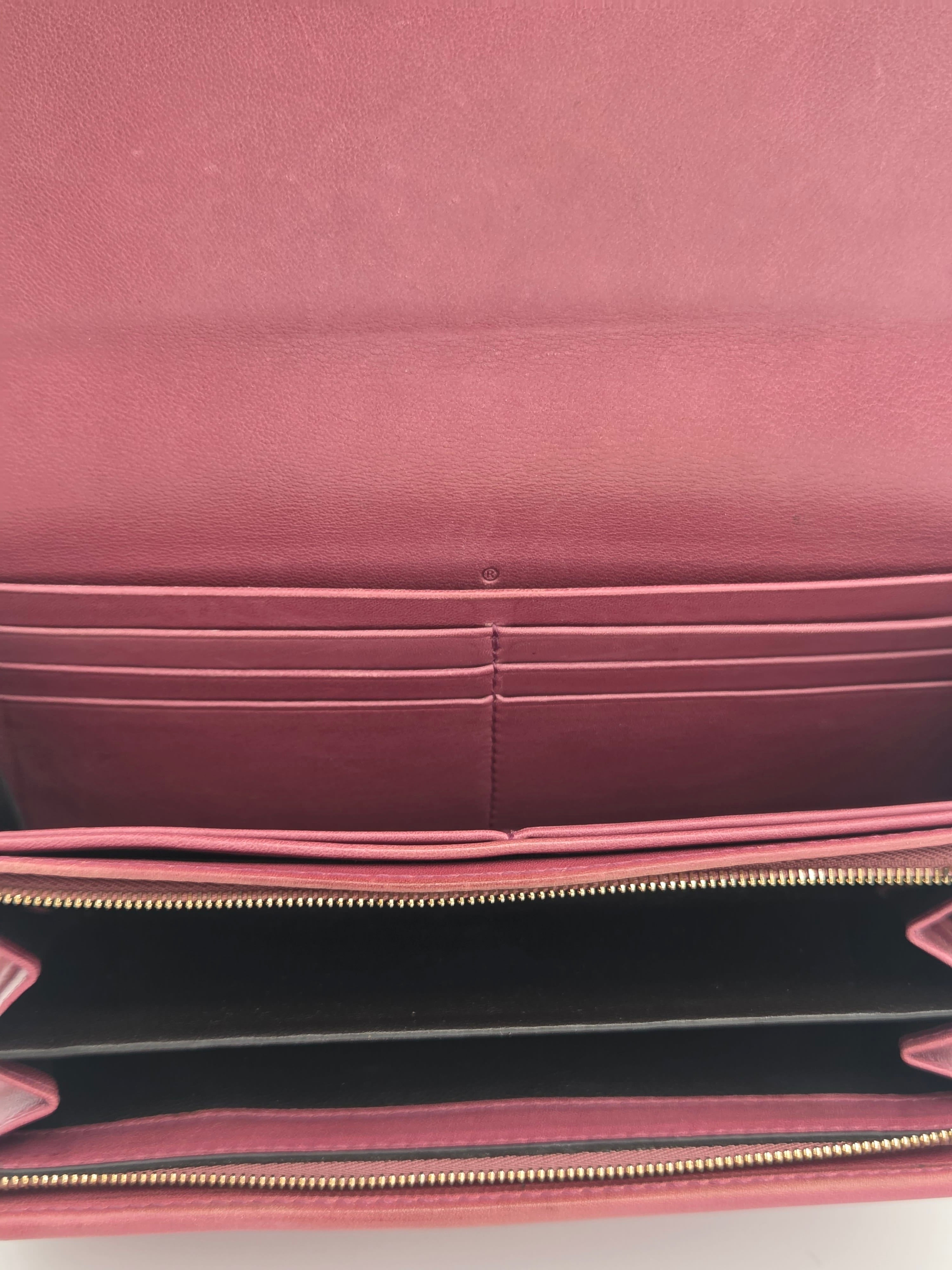 Close-up of the interior of a pink leather wallet or clutch, showing multiple card slots, a black interior lining, and a gold-tone zipper.