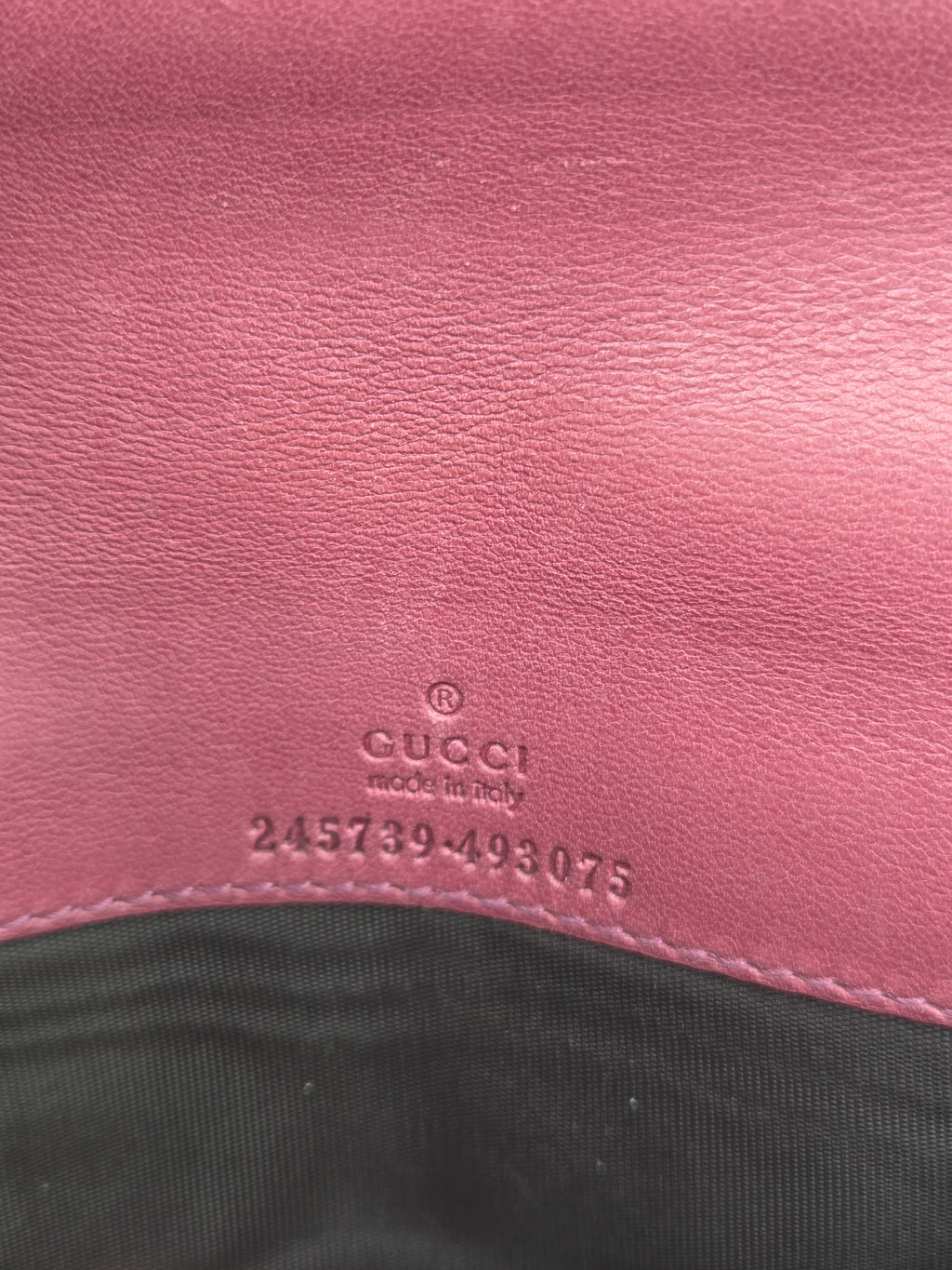 Close-up of a pink leather surface with embossed Gucci text and a black fabric section at the right edge.