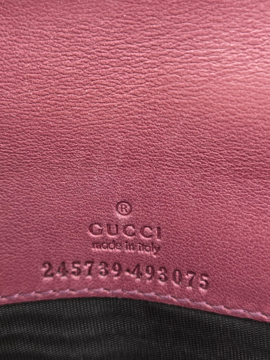 Close-up of a pink textured leather surface with an embossed GUCCI logo and 'made in Italy' text, next to a black fabric section.