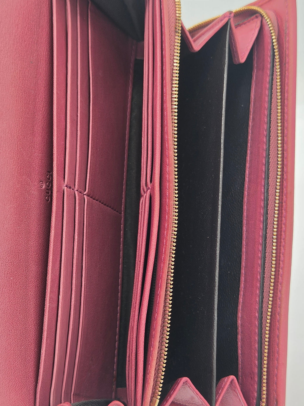 An open burgundy leather wallet showing its interior compartments, card slots, and gold-tone zippers.