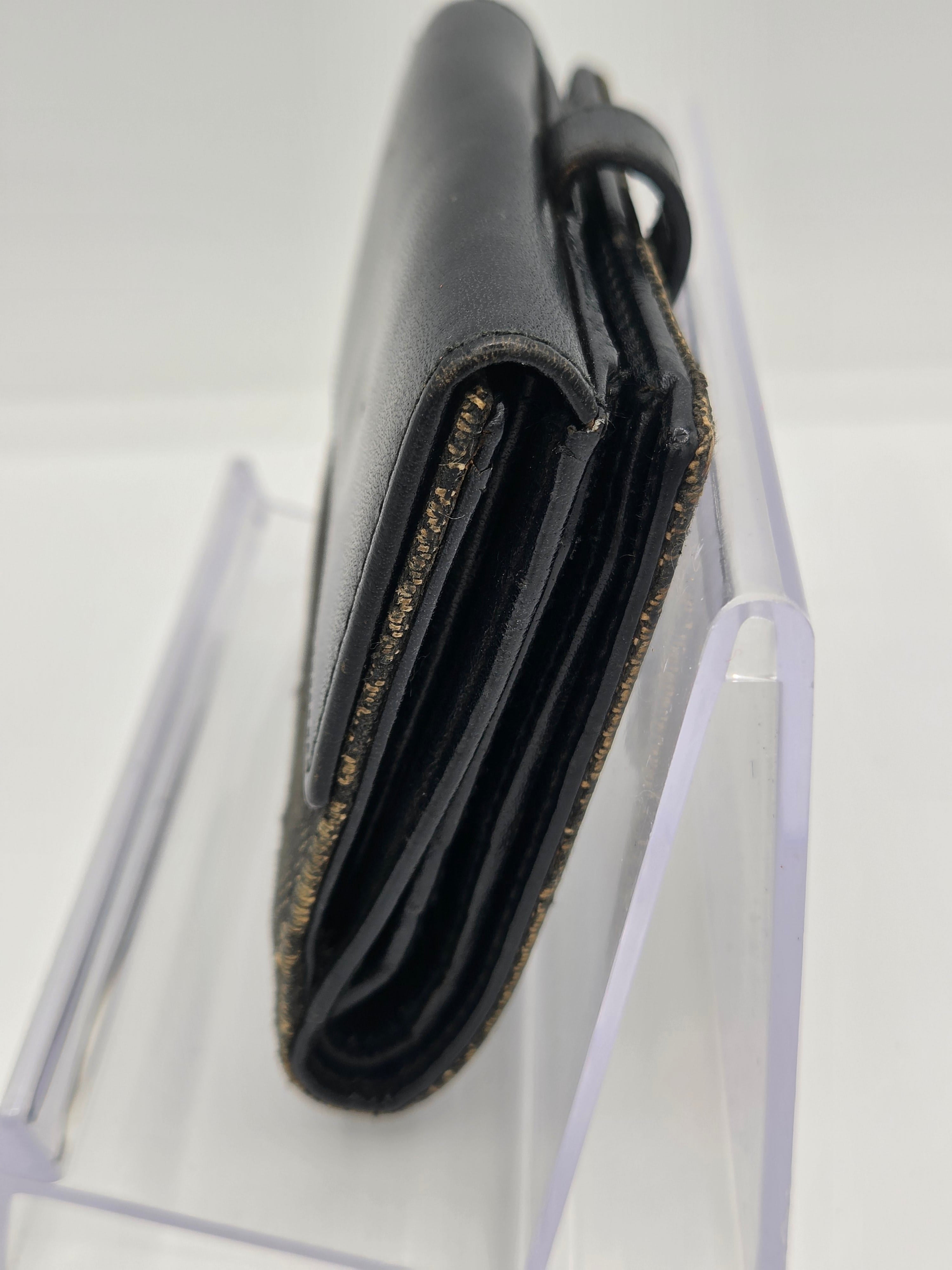 A close-up of a black leather wallet or card holder with gold glitter trim, shown resting on a clear acrylic display stand against a white background.