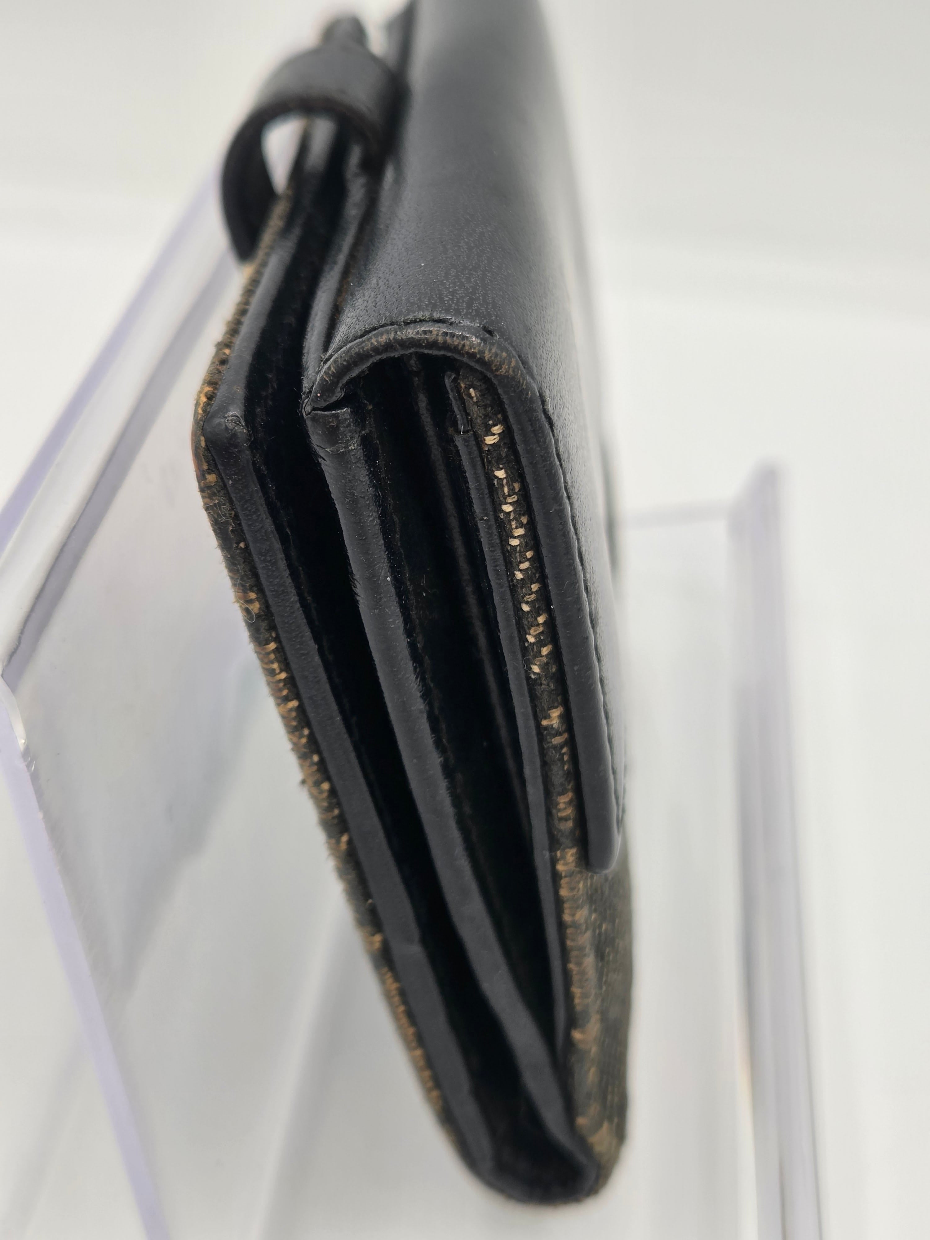 A close-up of a black leather wallet or card holder with gold glitter trim, resting on a clear acrylic stand against a white background.