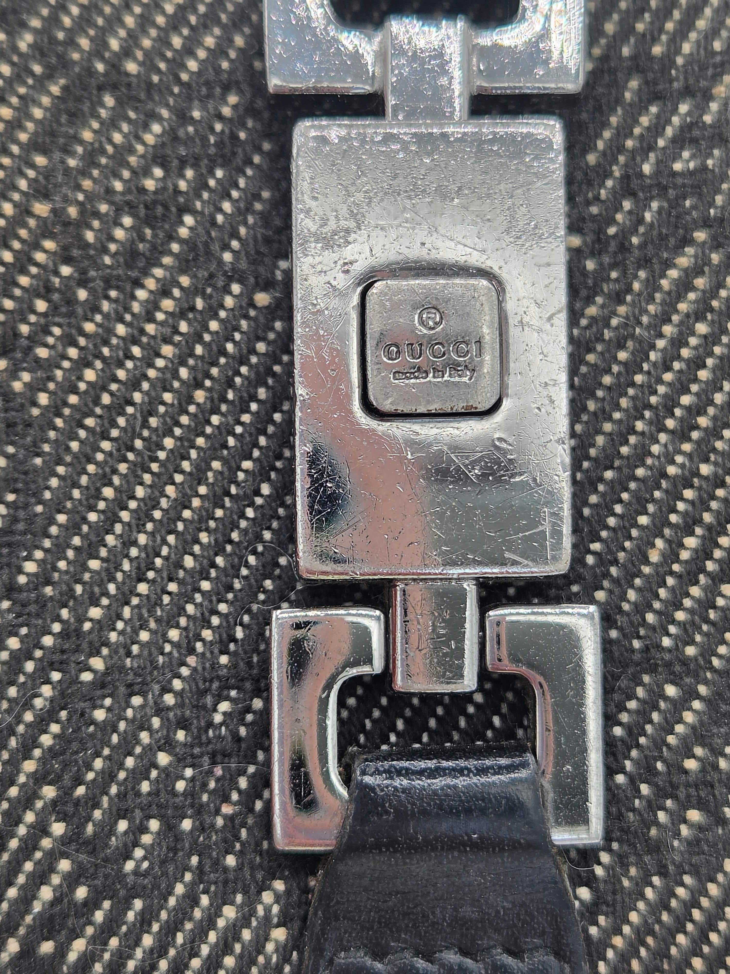 Close-up of a silver-toned metal clasp on a textured black and beige woven fabric, with a black strap visible on the right.