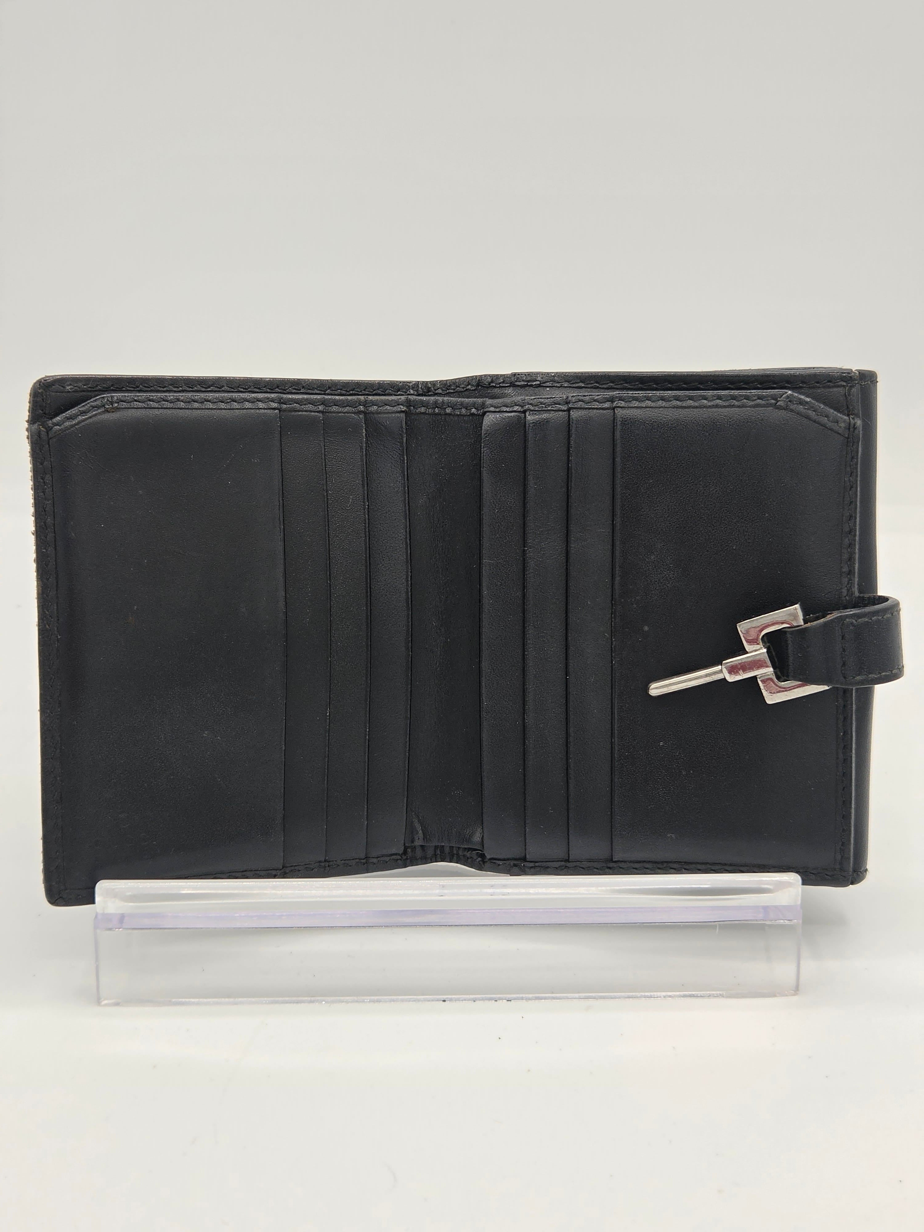 A black leather wallet with a silver-toned metal clasp closure, shown open next to a clear plastic protective sleeve on a plain white background.