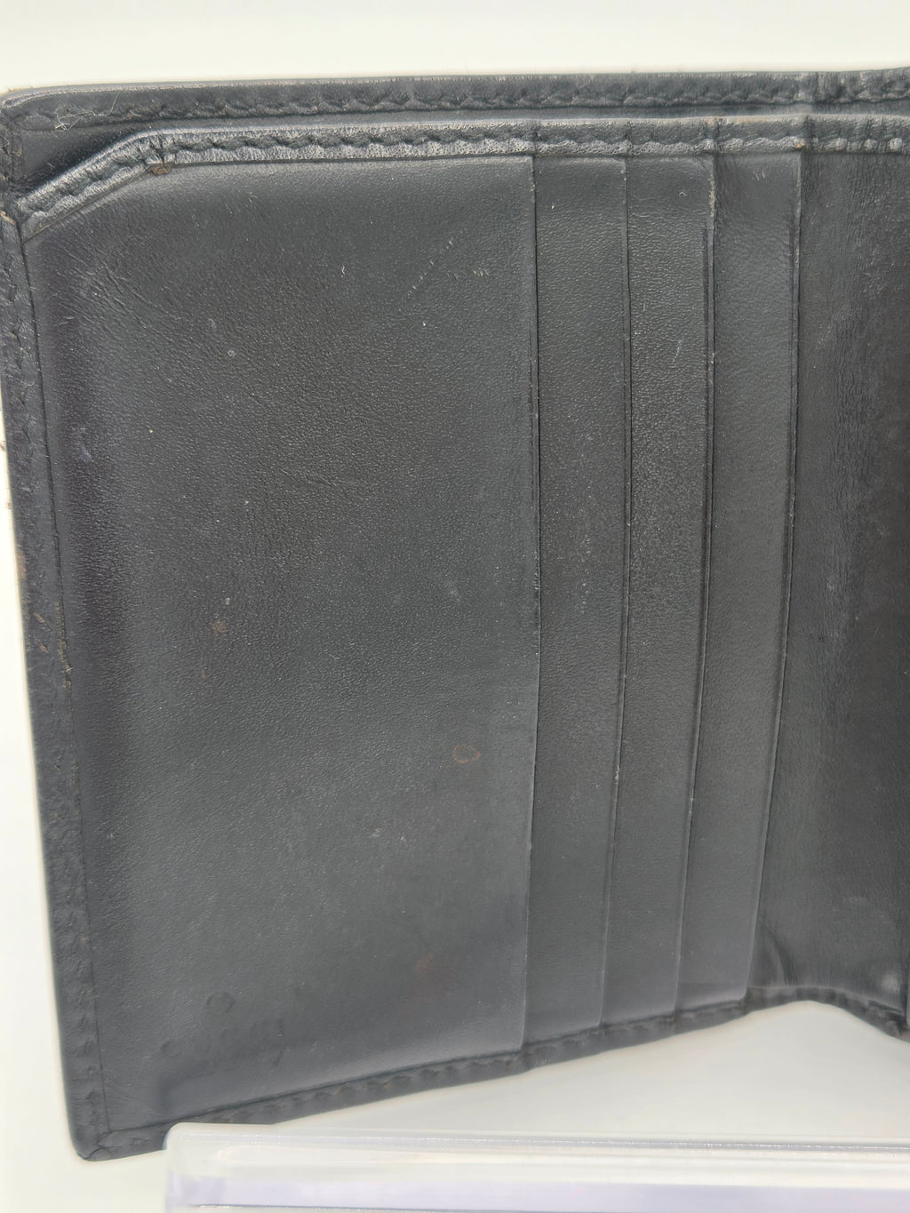 Close-up of the inside of a black leather wallet showing card slots and stitched edges on a white background.