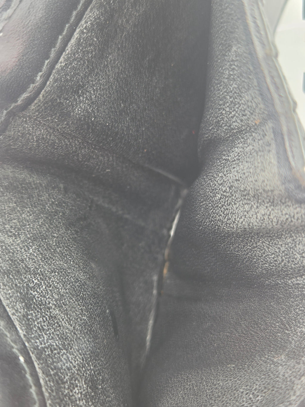Close-up of a black leather or faux-leather material with visible grain texture and stitched seams.