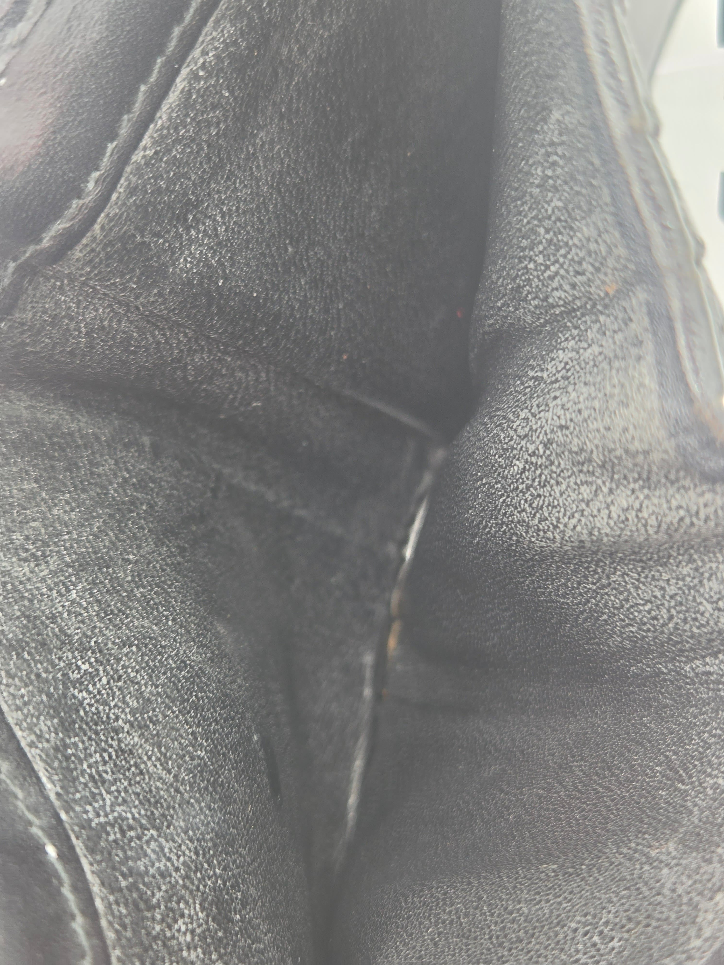 Close-up of a black leather or faux-leather material with visible grain texture and stitched seams.