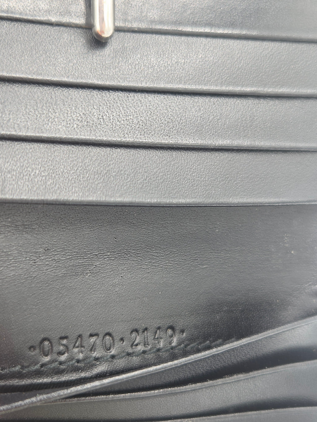 Close-up of a black leather accessory showing vertical stitched panels, a metal ring on the left, and embossed numbers on the right.