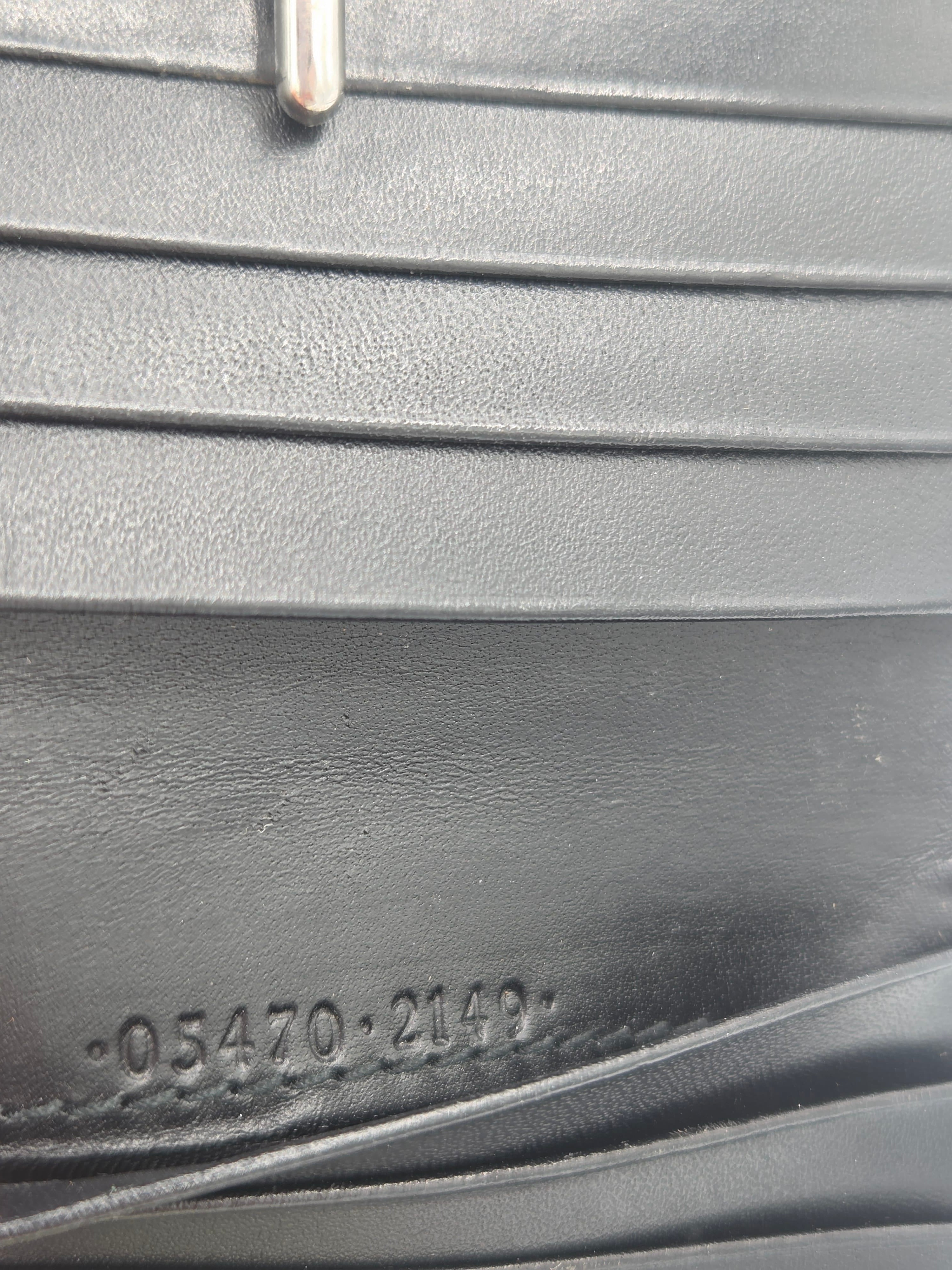 Close-up of a black leather accessory showing vertical stitched panels, a metal ring on the left, and embossed numbers on the right.