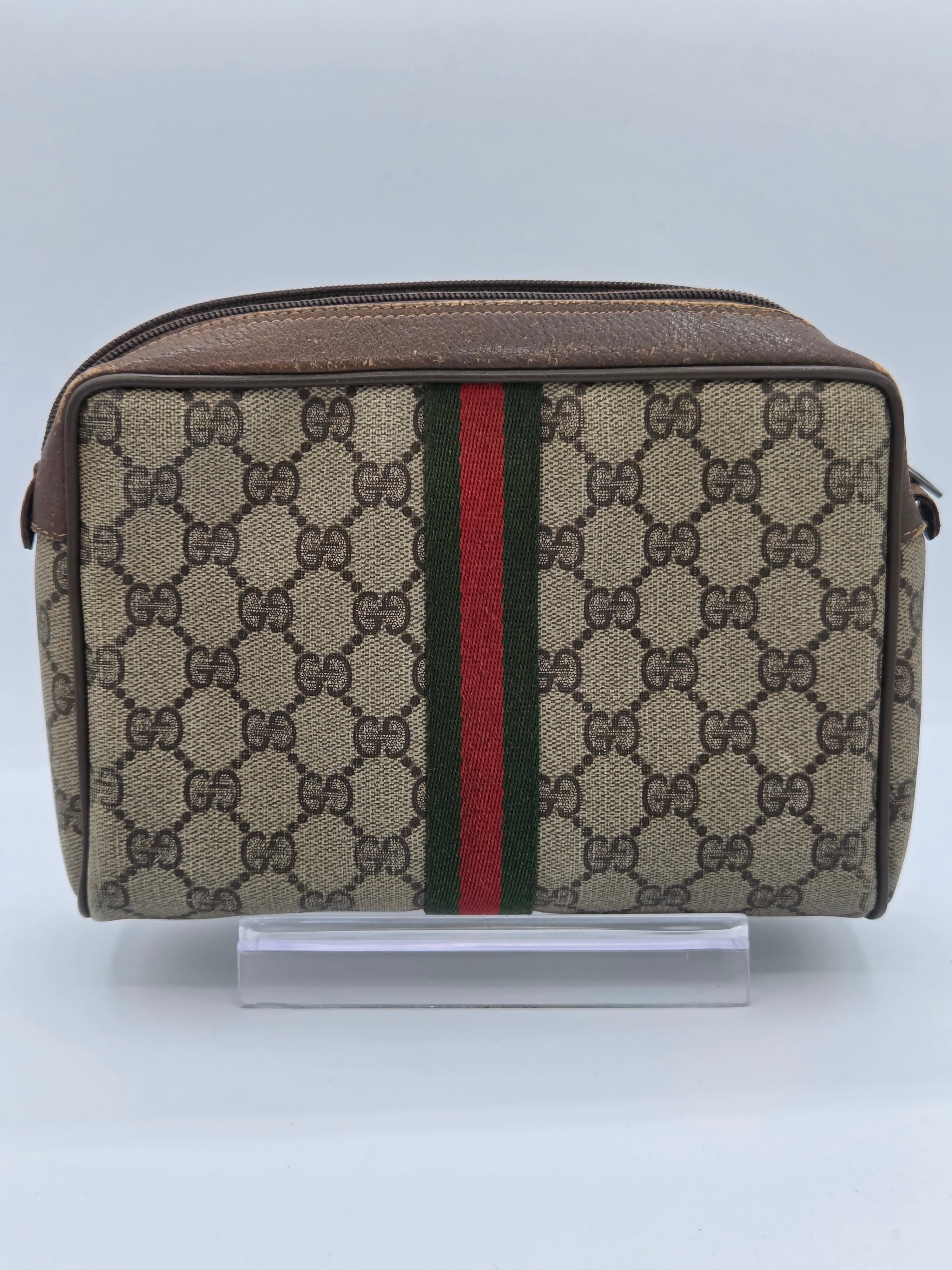 A Gucci monogram canvas pouch with a brown leather trim and the signature green and red web stripe, shown against a plain light background.