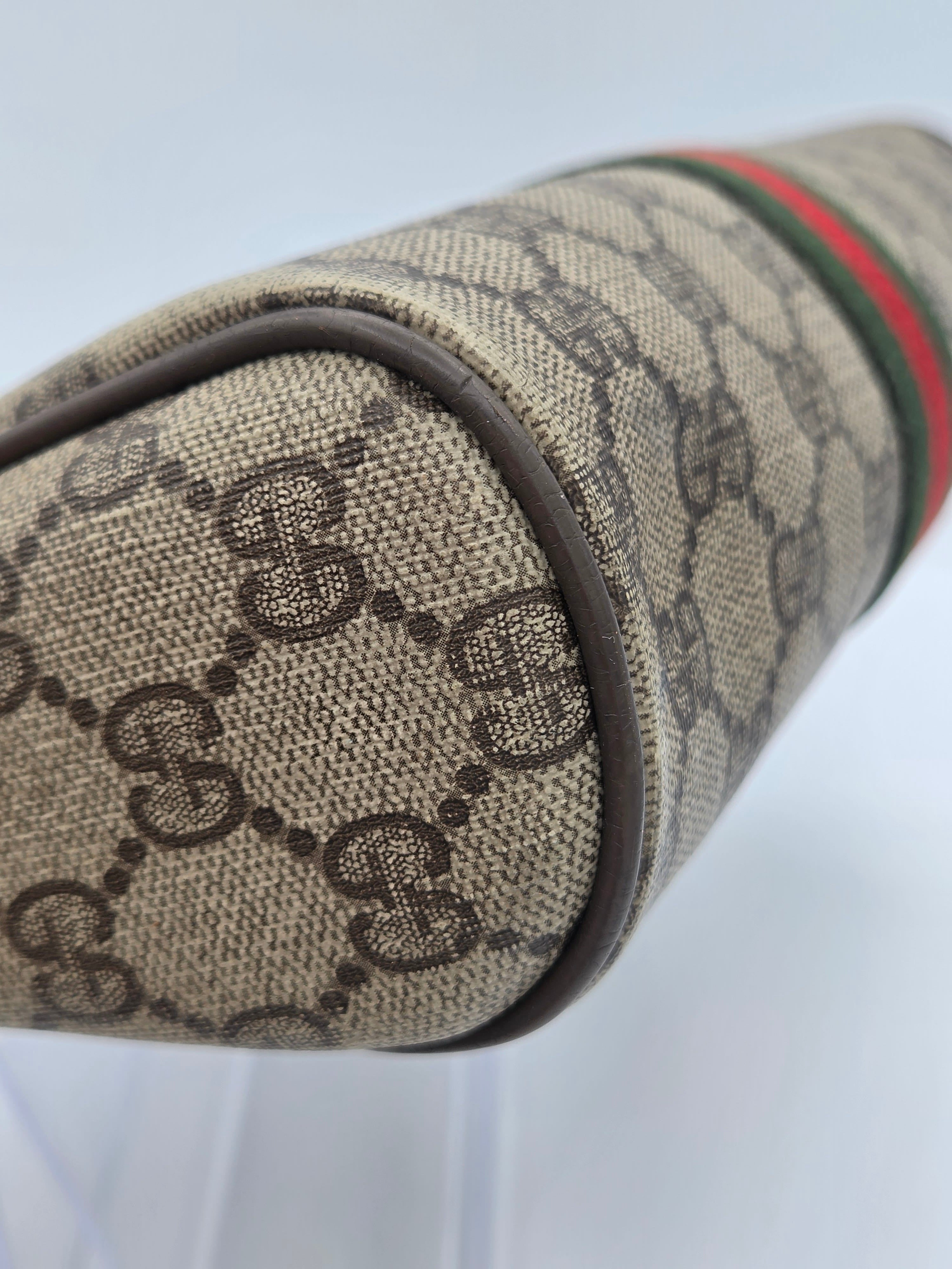 Close-up of a Gucci monogram canvas bag corner showing the beige and brown GG pattern, dark brown trim, and the signature green and red web stripe near the top.