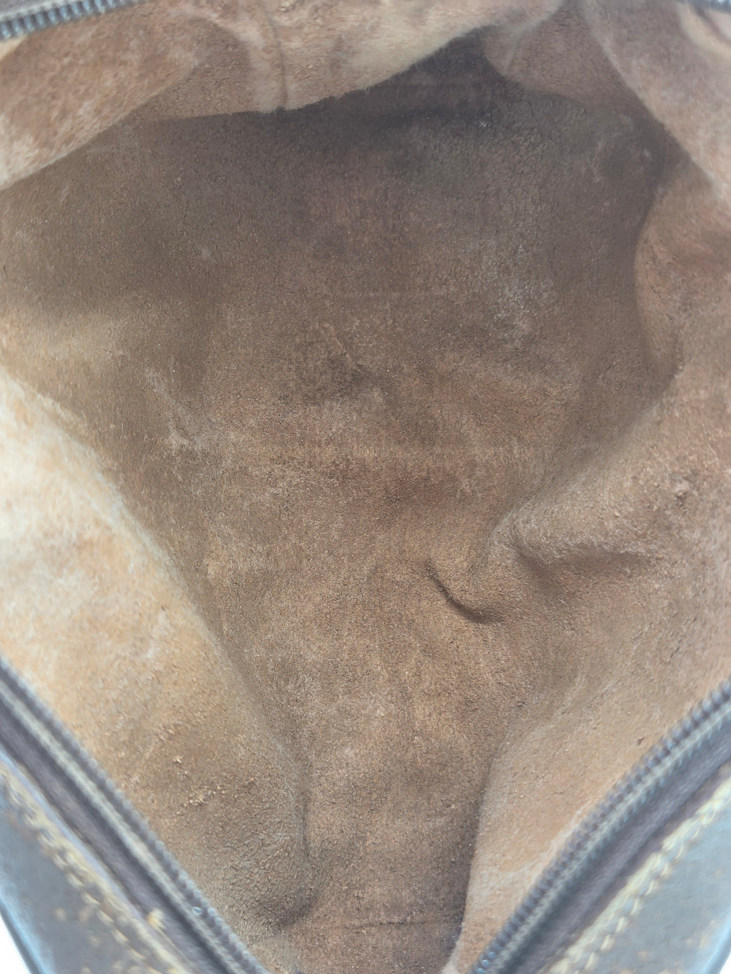 Close-up view of the interior lining of a bag or pouch, showing a brown suede or microfiber material with a zipper edge visible at the top and sides.