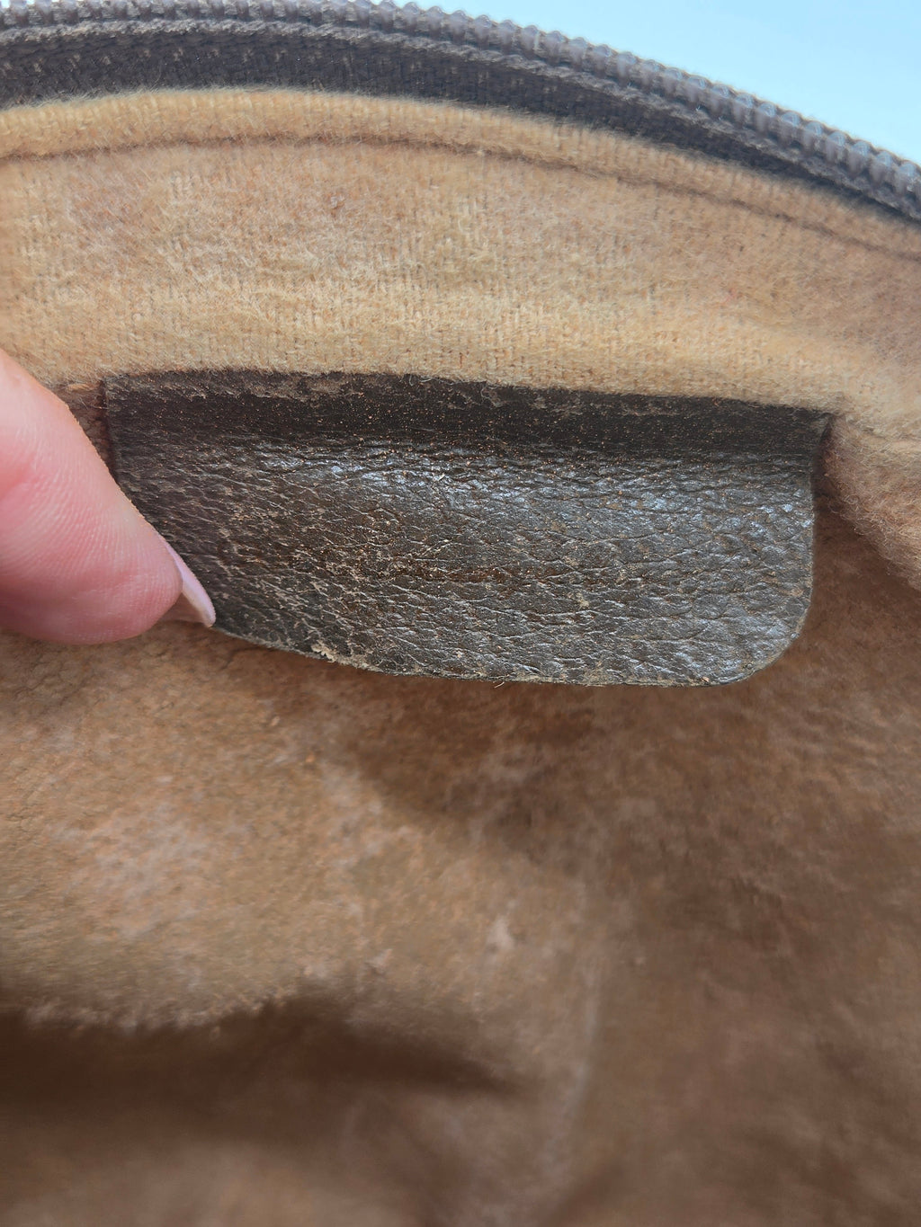 Close-up of a tan suede or microfiber fabric surface with a dark brown textured rectangular patch and part of a finger visible at the bottom edge.