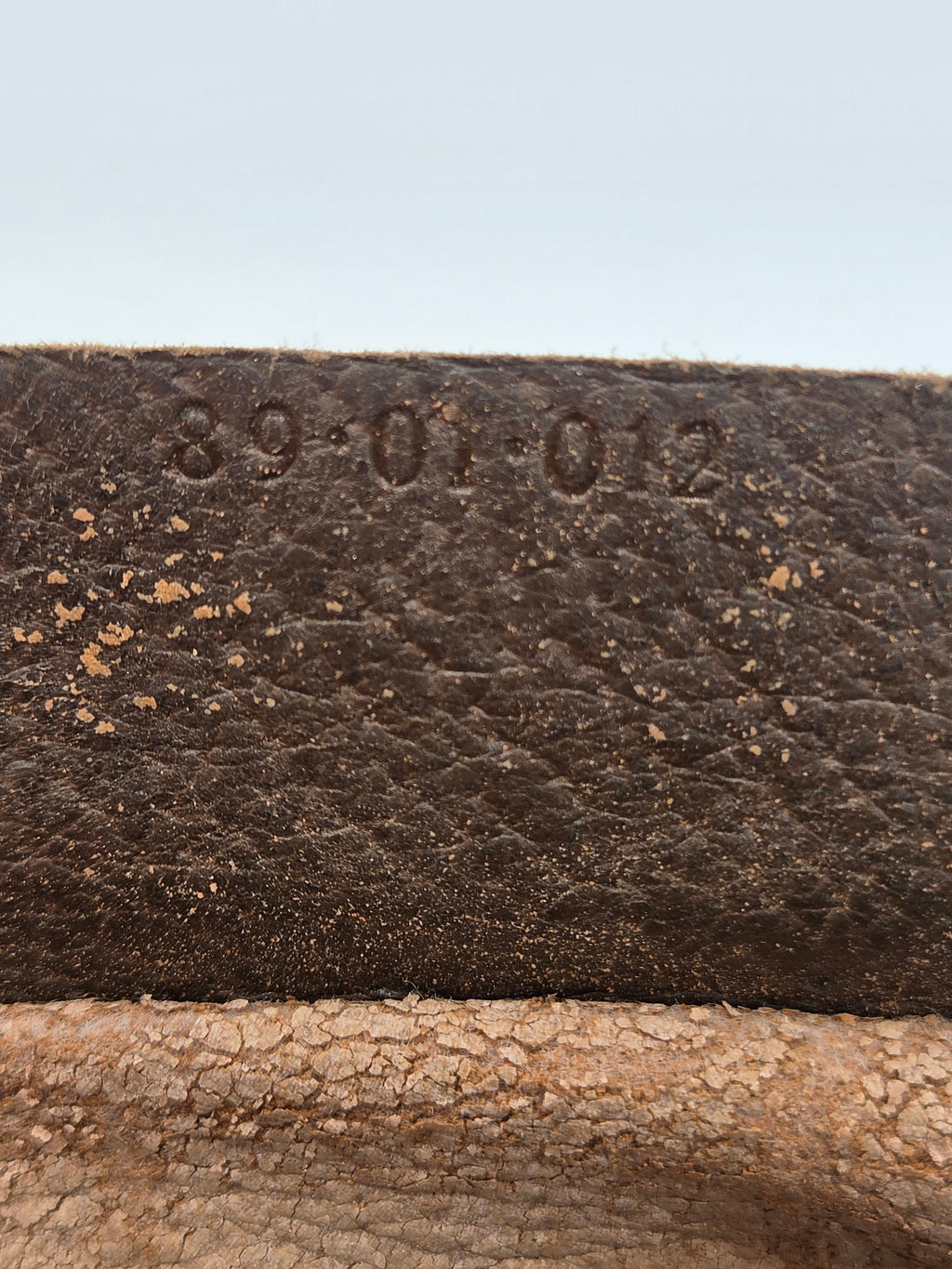 Close-up of a dark brown textured leather strap or material with embossed numbers '89-01-02' on the left side, next to a lighter tan textured surface.