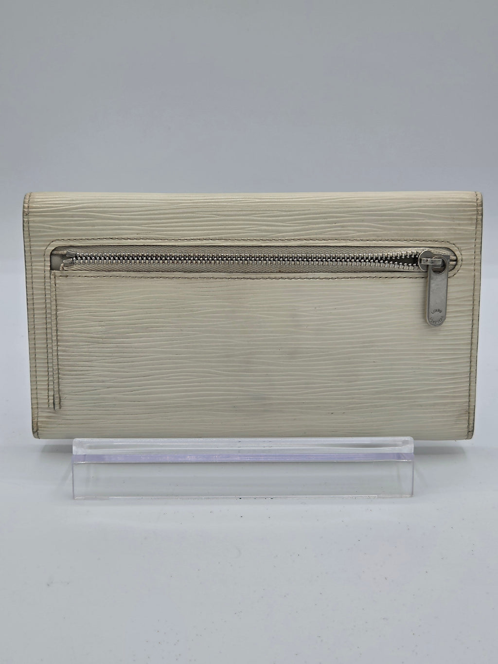A beige textured leather zip-around wallet or notebook cover with a silver metal zipper pull, shown against a plain light gray background.