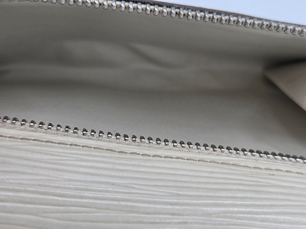 Close-up of a light gray textured leather clutch or wallet showing the interior lining and silver-tone bead trim along the zipper.