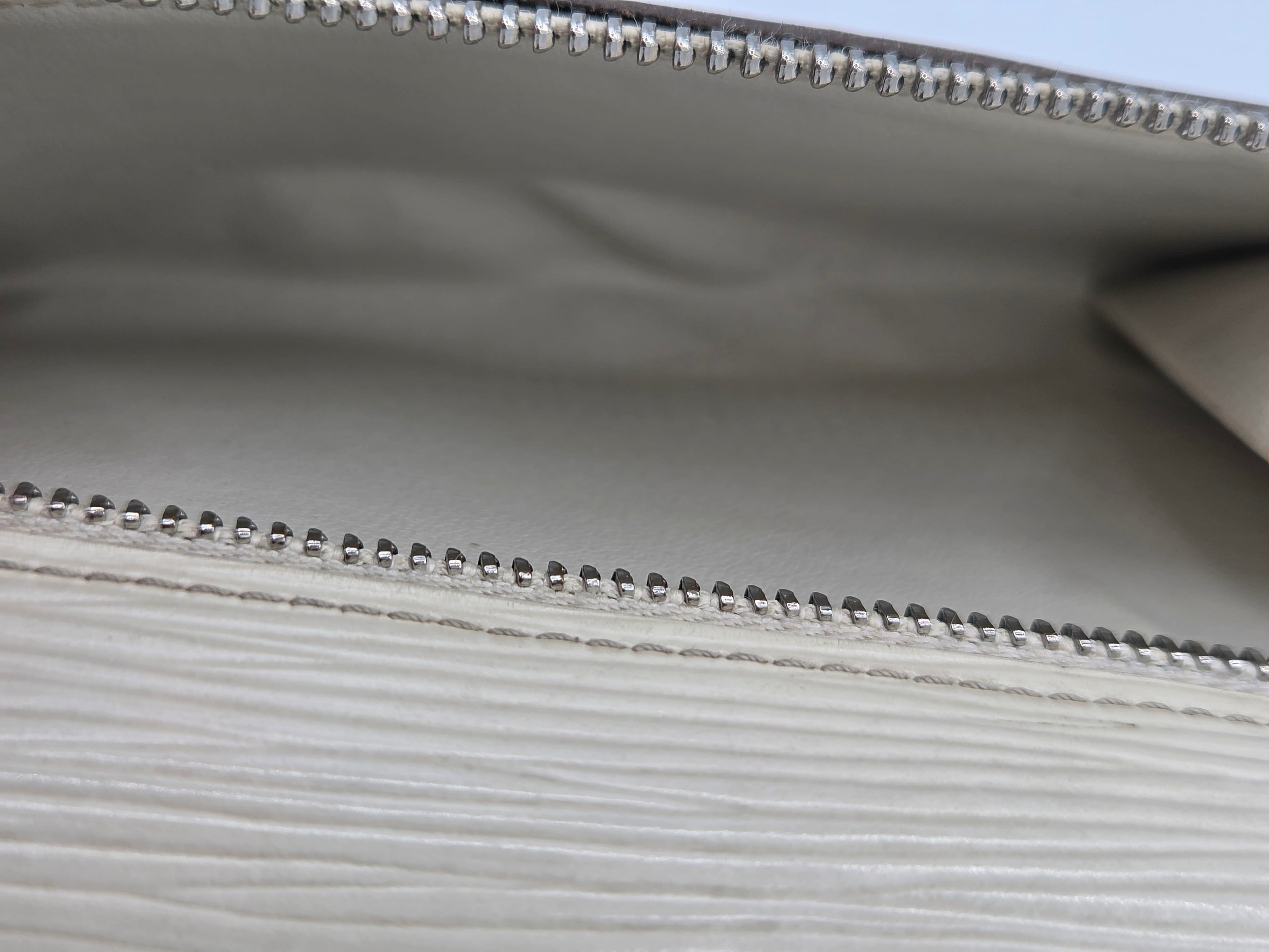 Close-up of a light gray textured leather clutch or wallet showing the interior lining and silver-tone bead trim along the zipper.