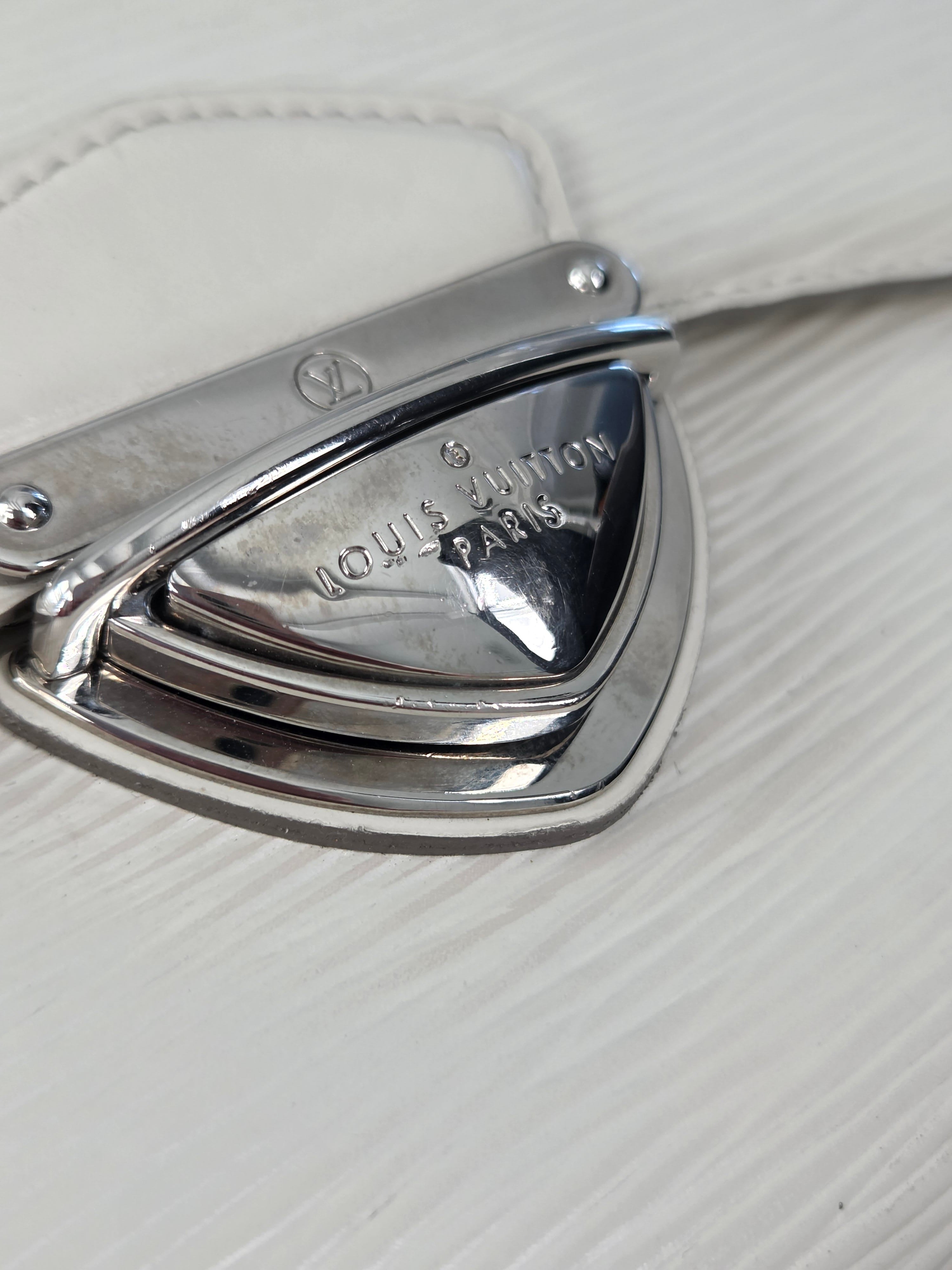 Close-up of a polished silver metal Louis Vuitton monogrammed clasp on a textured white leather surface.