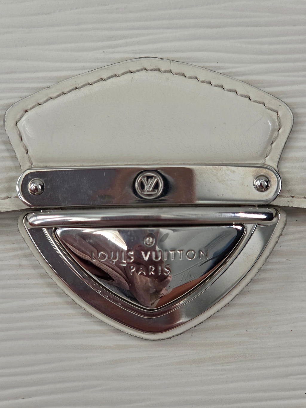 Close-up of a Louis Vuitton metal clasp and white leather strap on a textured white surface.