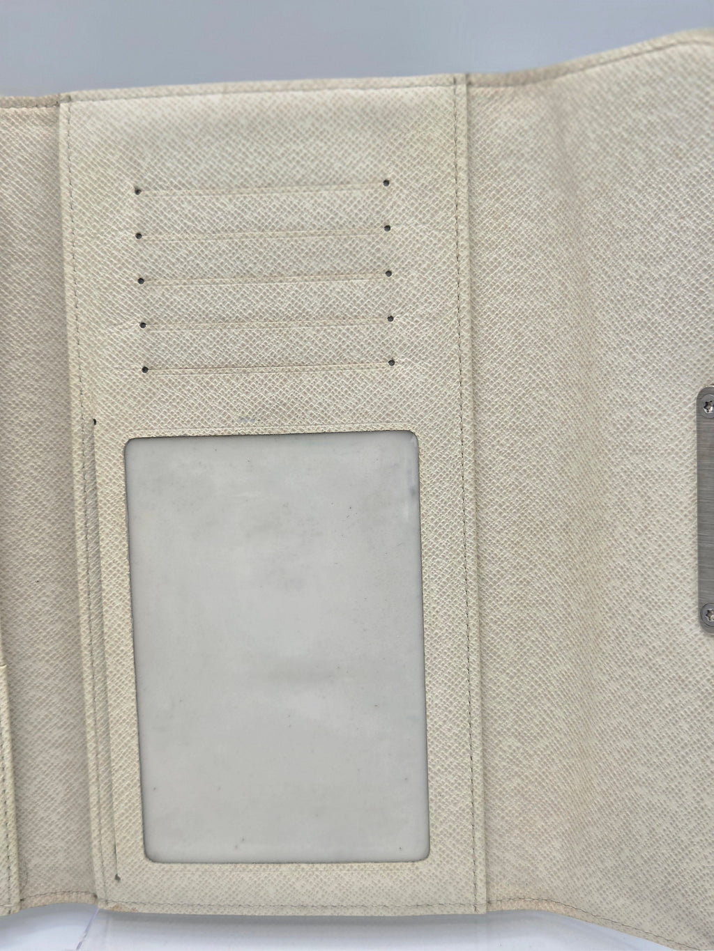 Close-up of the interior of a textured cream-colored wallet or organizer, showing card slots on the left and a clear ID window on the right.