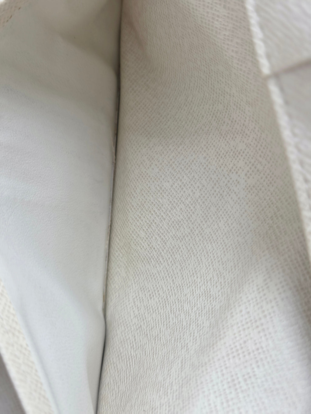 Close-up of a light beige woven fabric with a fine textured weave, folded to show its texture and stitching.