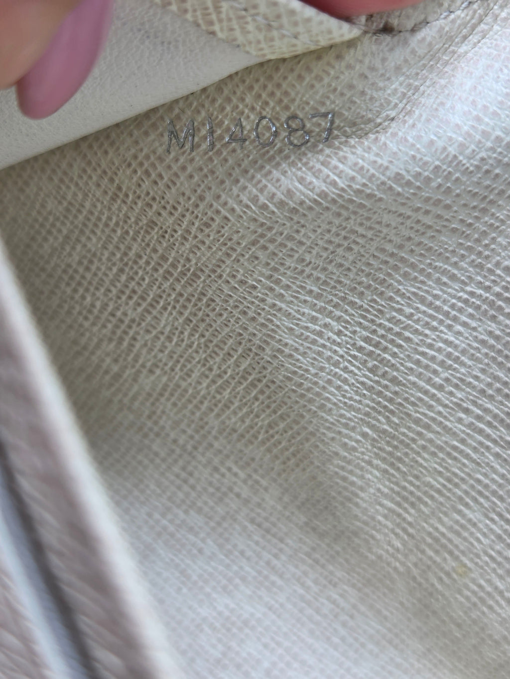 Close-up of a light beige woven fabric surface with a small vertical stamped code and a partial pink finger visible at the left edge.