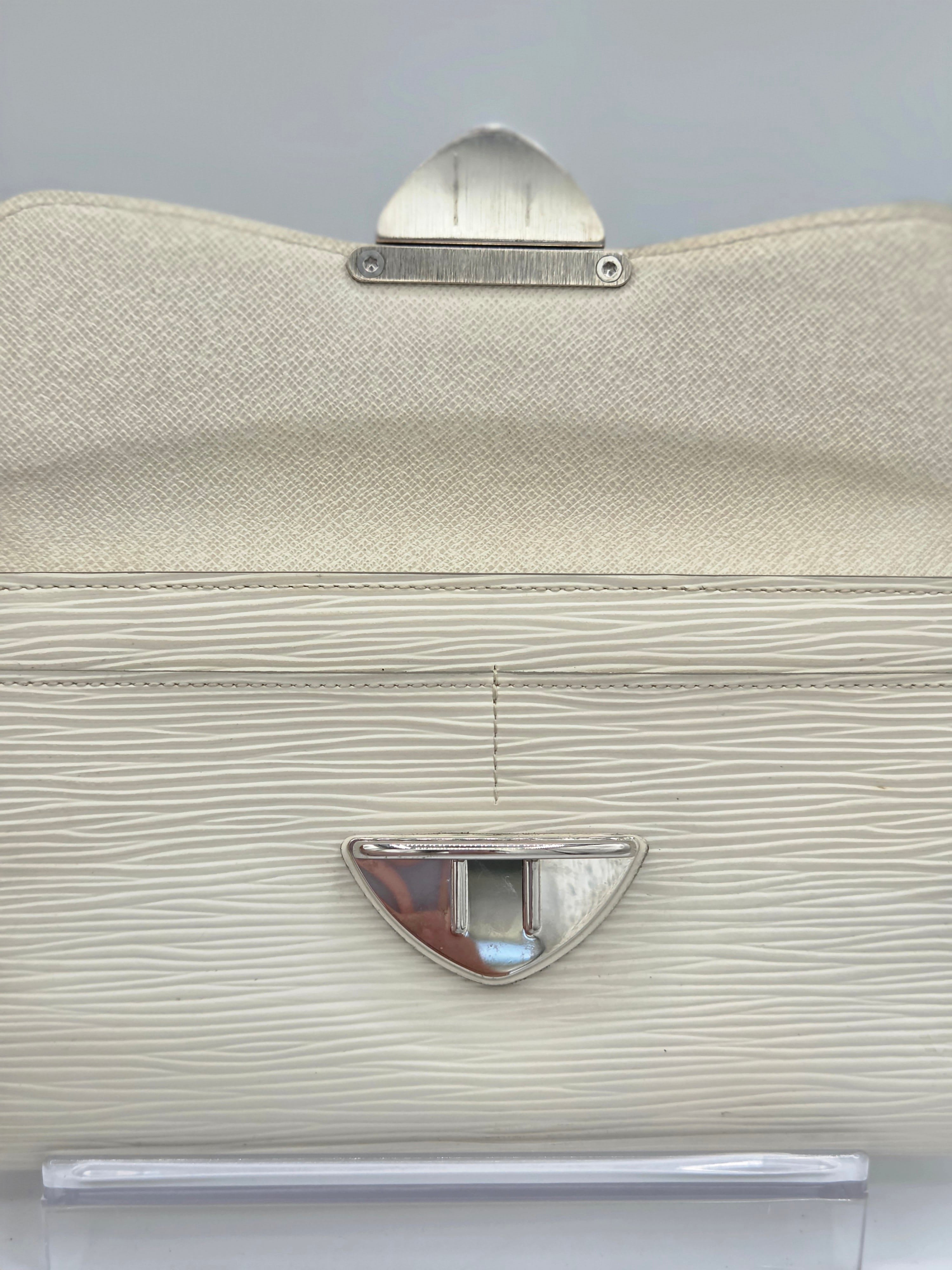 A close-up of a structured handbag in textured cream-colored leather with silver-tone metal hardware, including a top clasp and a central lock.