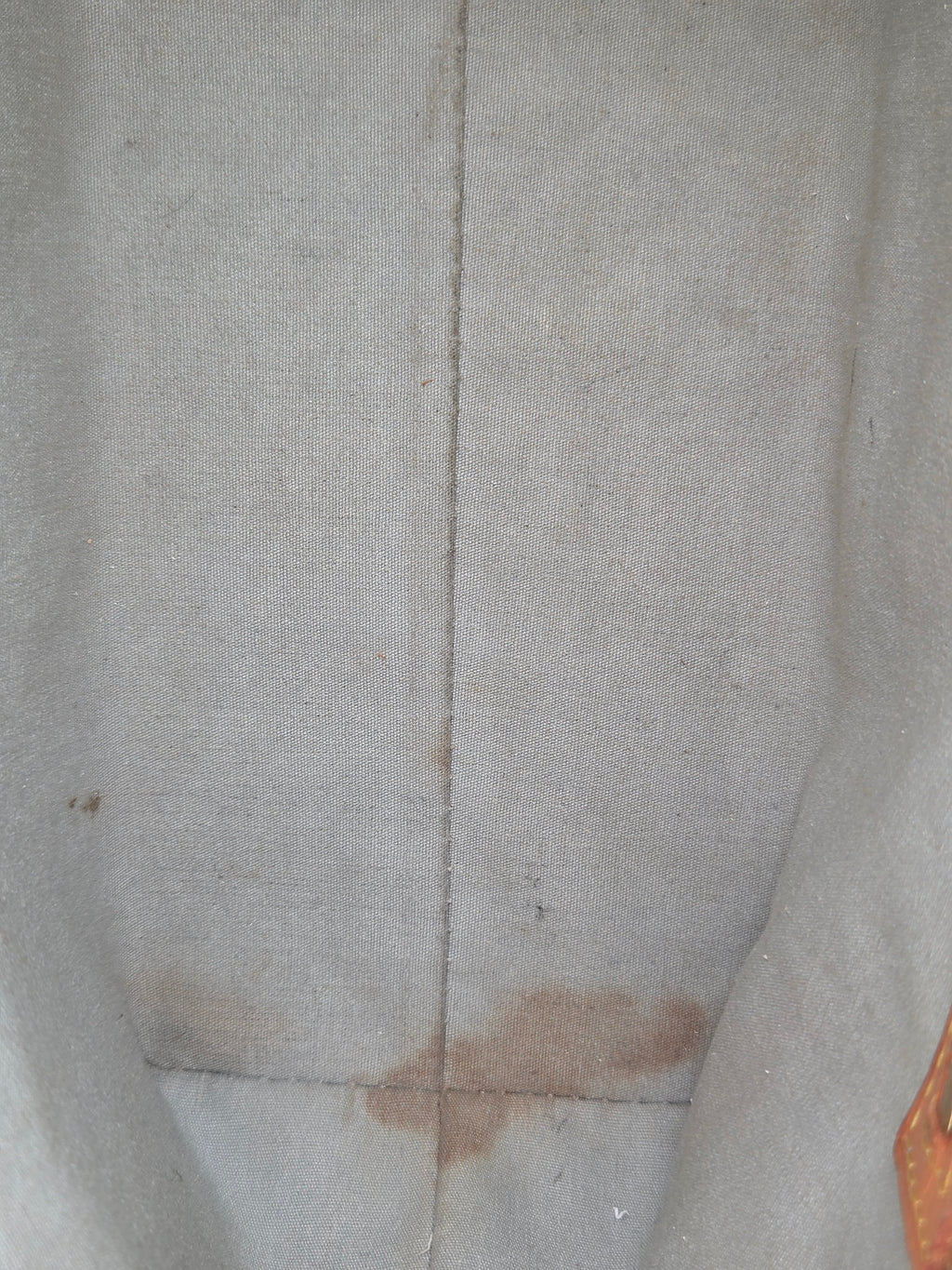 Close-up of a light beige or off-white textured fabric surface with a vertical seam and a brown stain or patch near the bottom center.