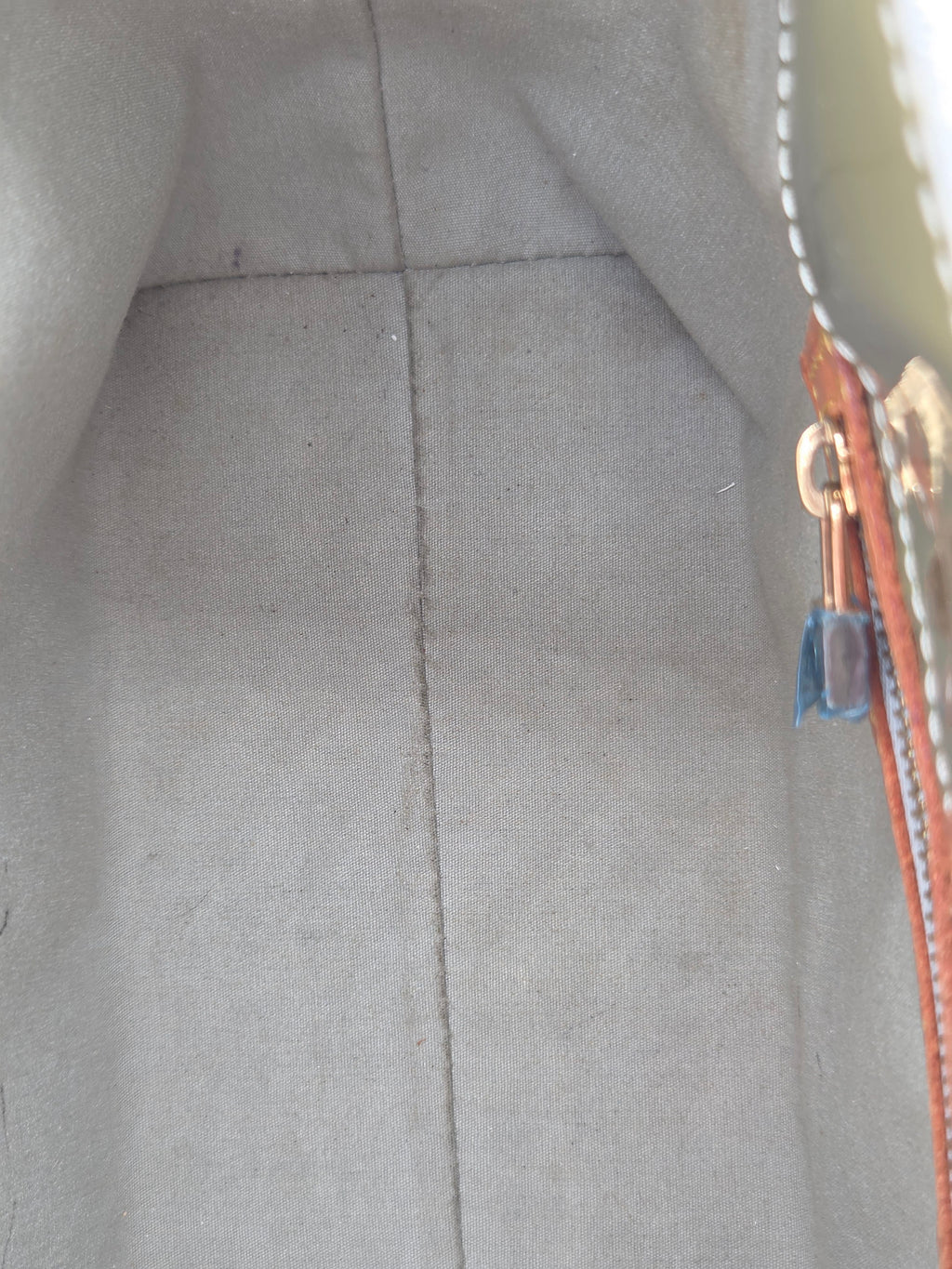 Close-up of the interior lining of a light gray fabric bag, showing a zipper with a brown leather pull tab and gold-tone hardware.