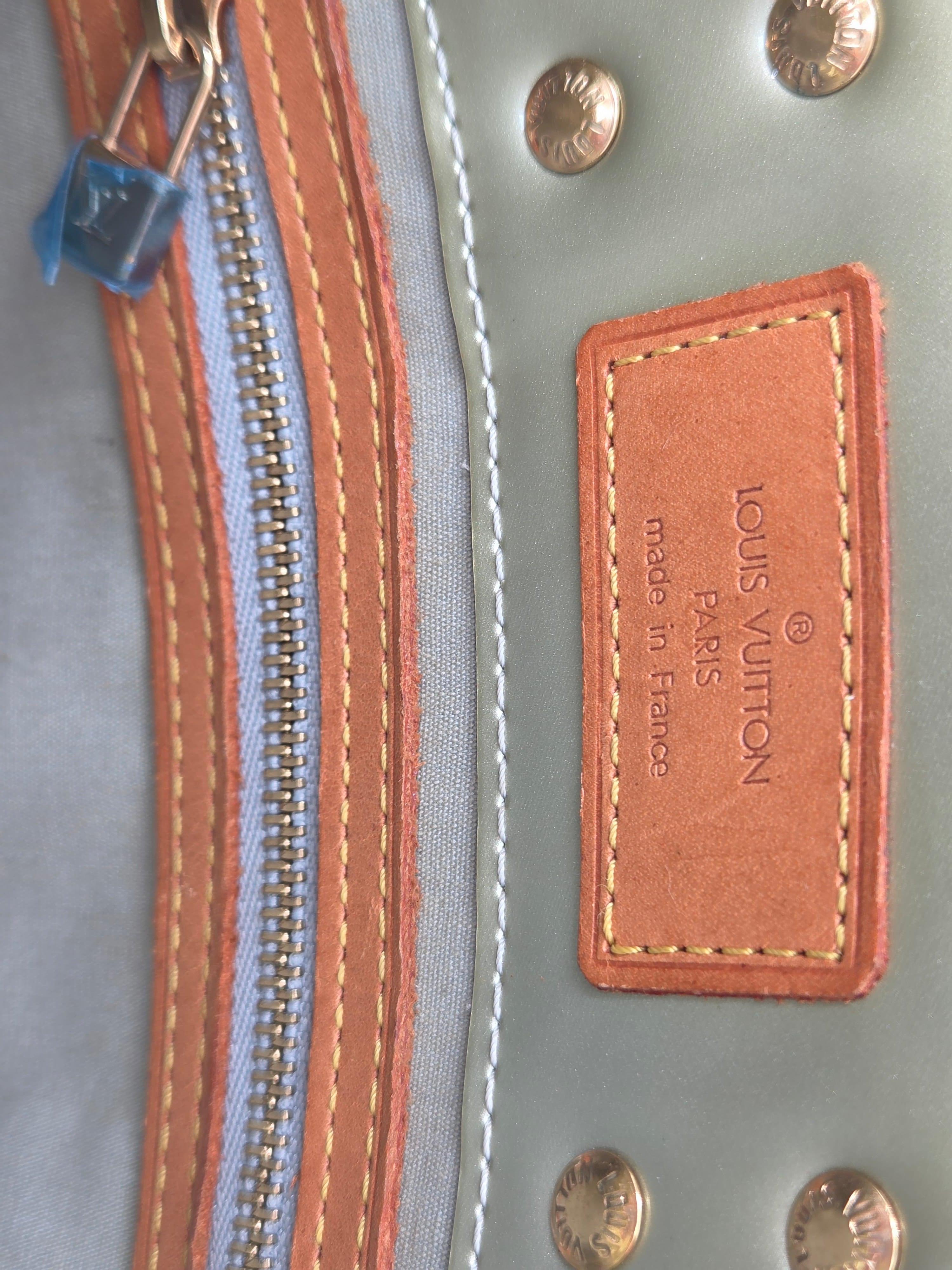 Close-up of a Louis Vuitton handbag interior showing a tan leather patch with 'LOUIS VUITTON PARIS made in France' text, a blue zipper pull, and a light blue-gray fabric body with brass studs.